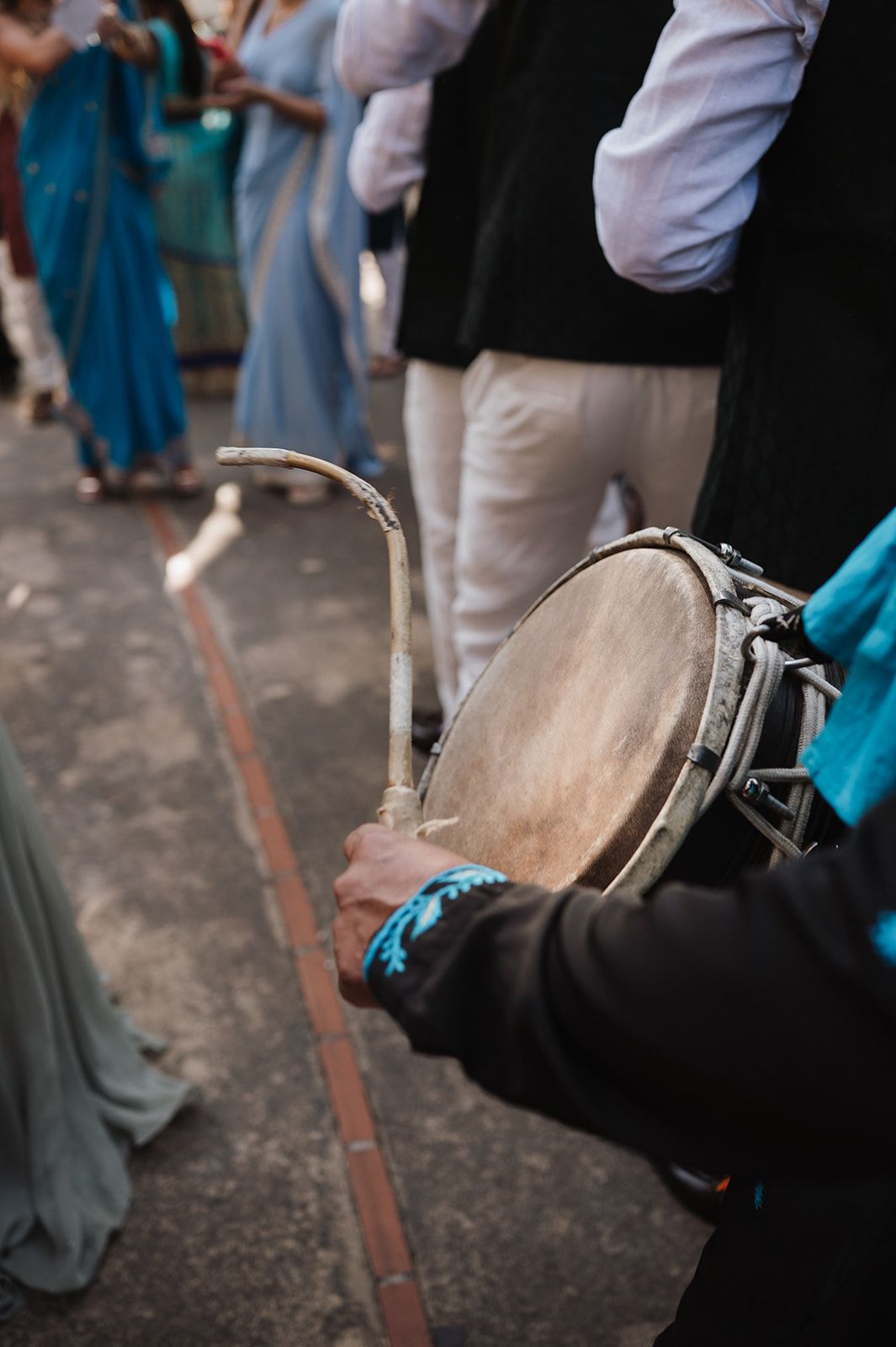 Musician playing a traditional hand drum at an Indian wedding celebration outdoors.