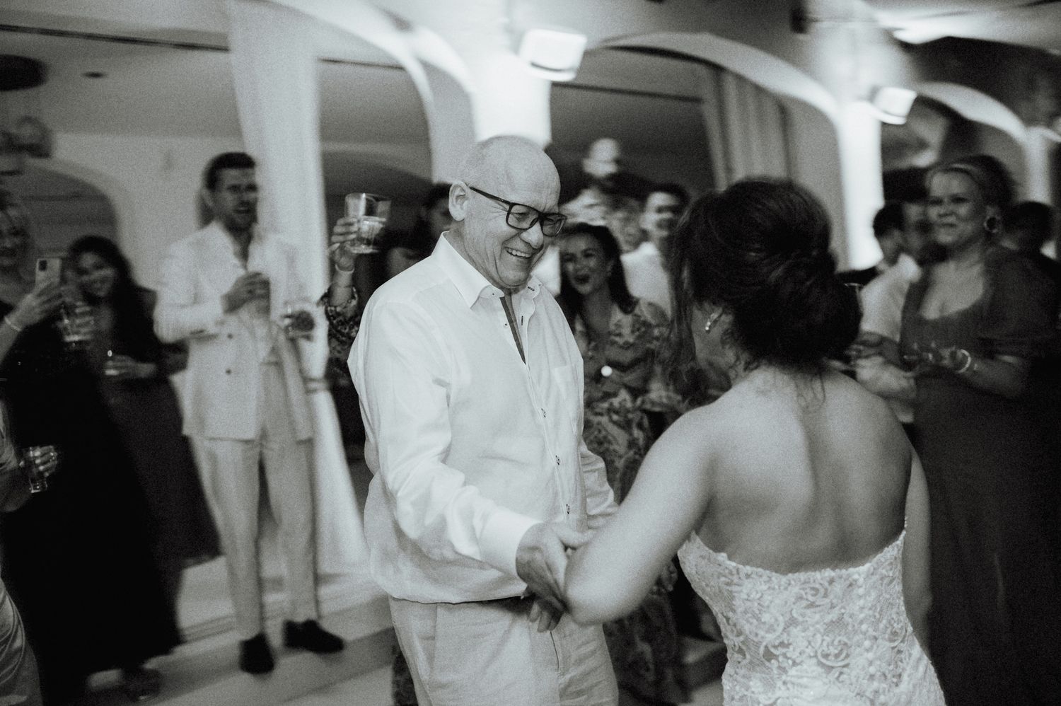 Elegantly dressed older gentleman dances with the bride at a festive wedding reception celebration.
