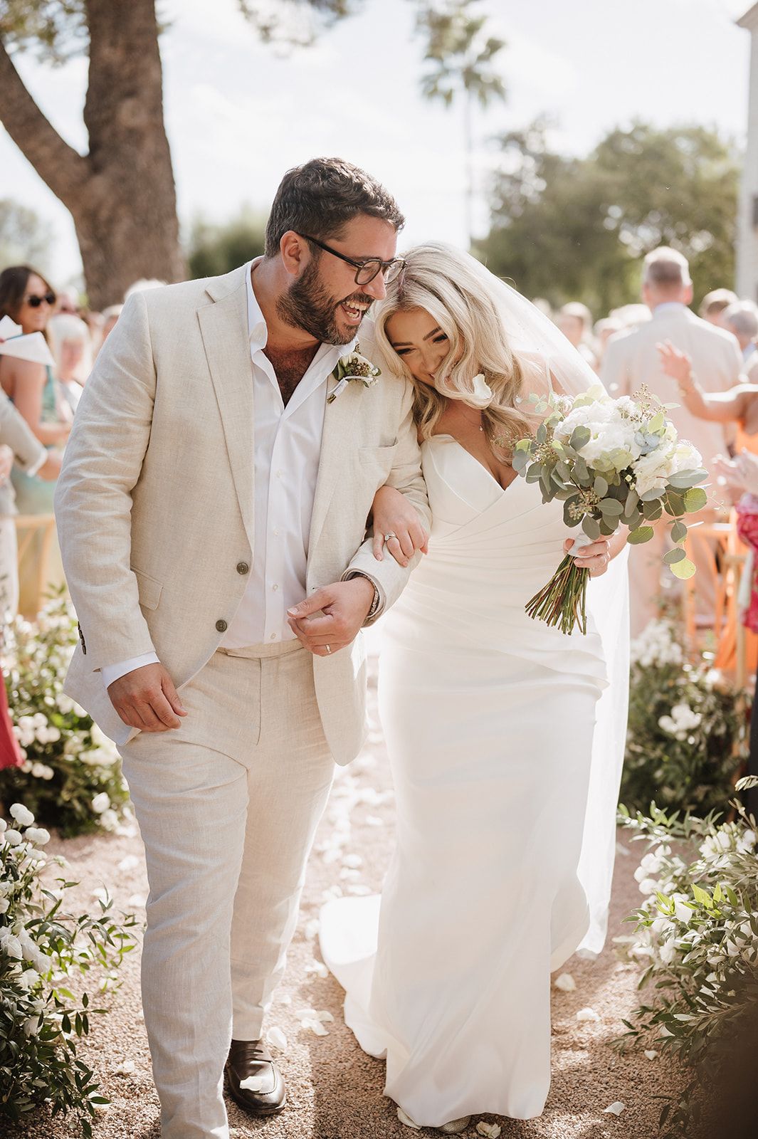 Newlyweds walking down aisle, bride in white gown holding blue bouquet.
