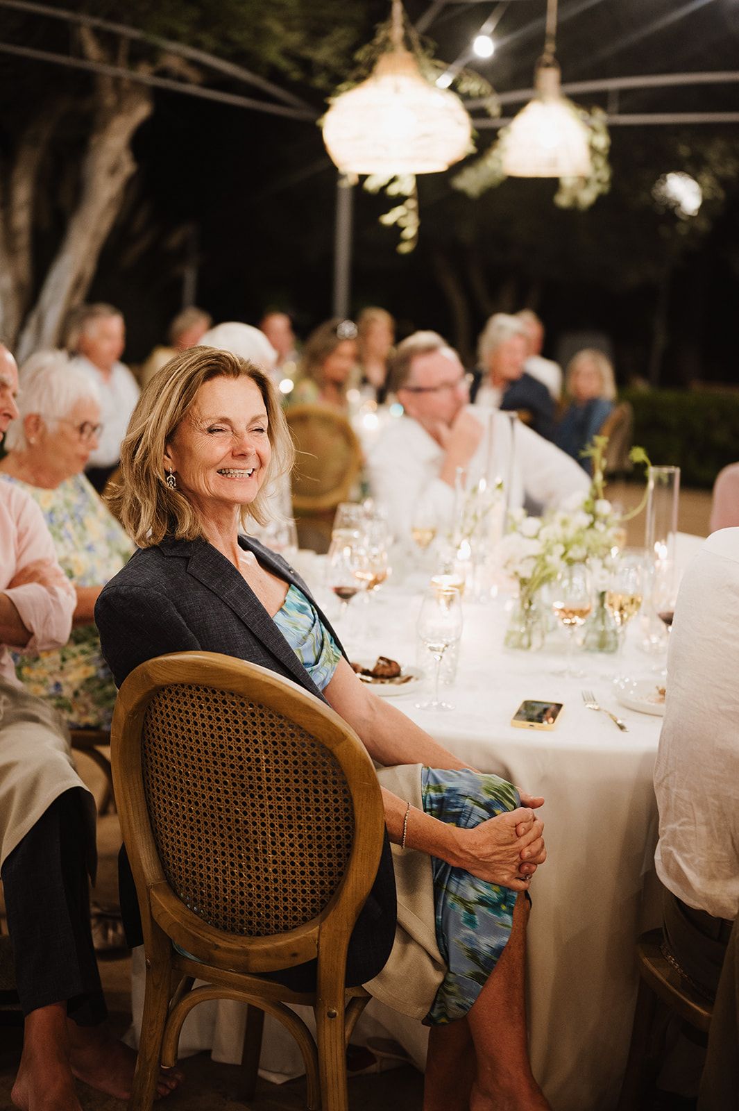 Elegant woman smiling at outdoor evening wedding reception dinner under warm string lights.
