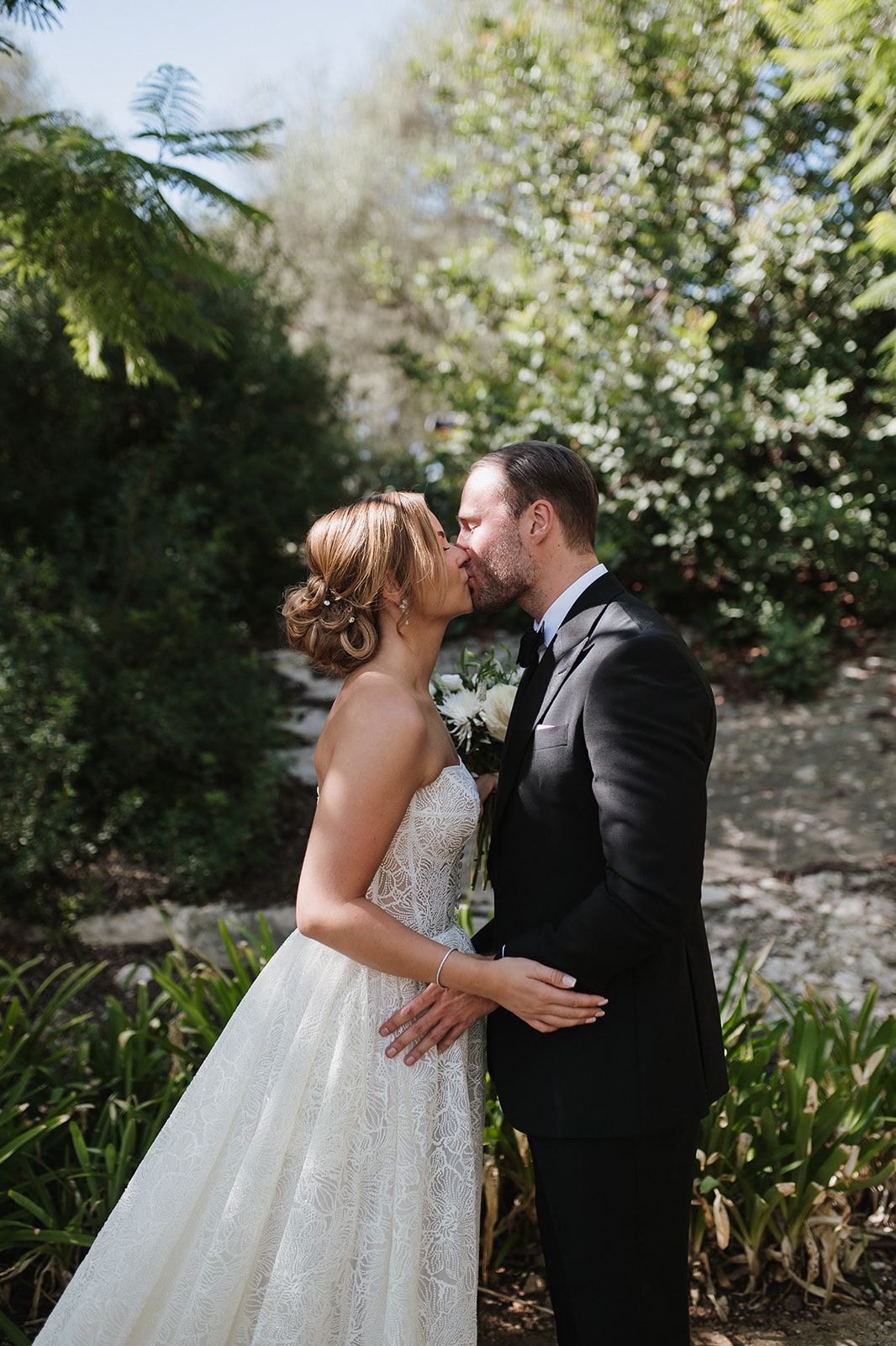 Bride and groom sharing romantic kiss in lush garden on wedding day.