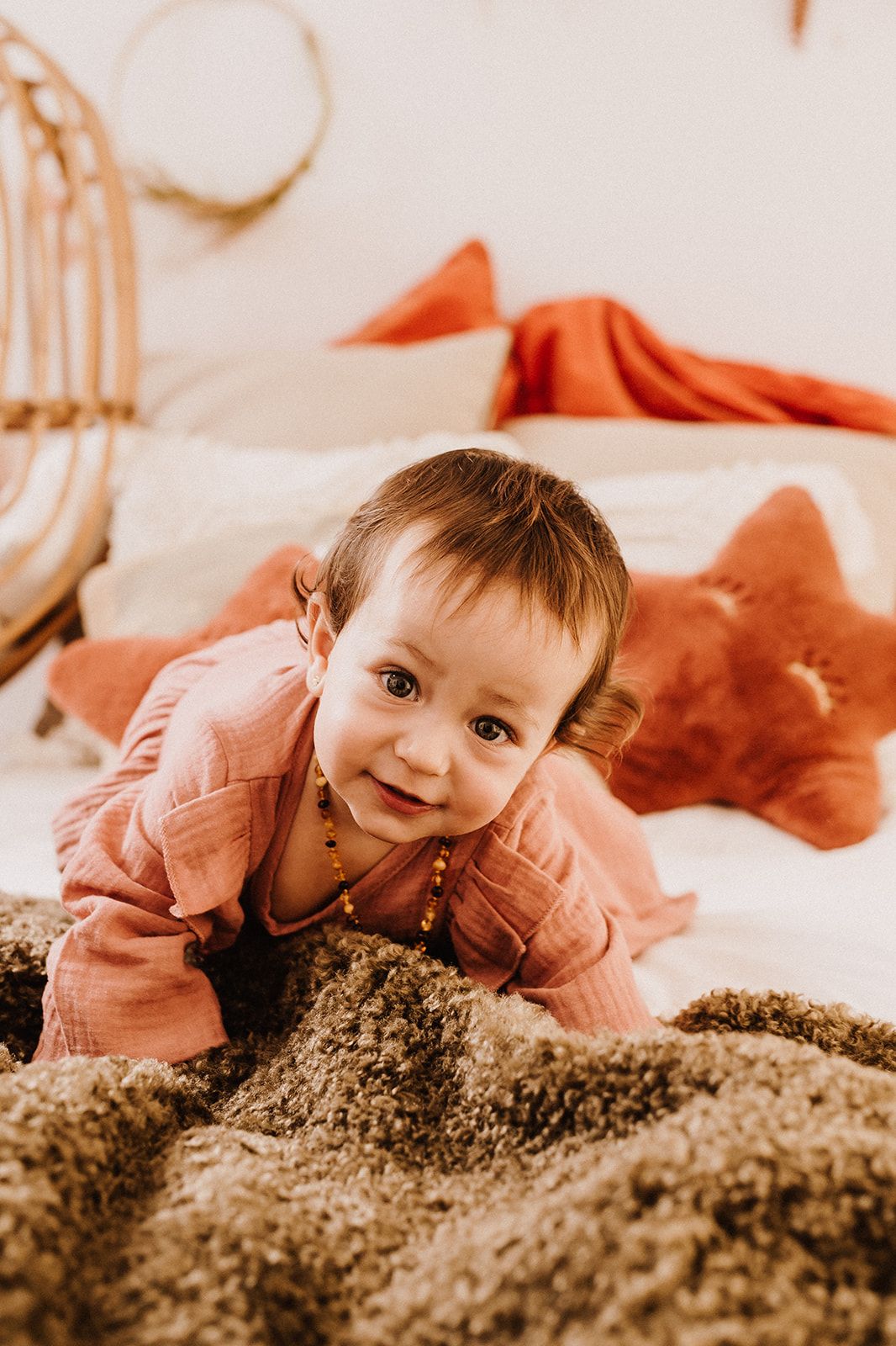 Smiling baby in pink outfit doing tummy time on a fluffy brown blanket with boho bedroom decor.