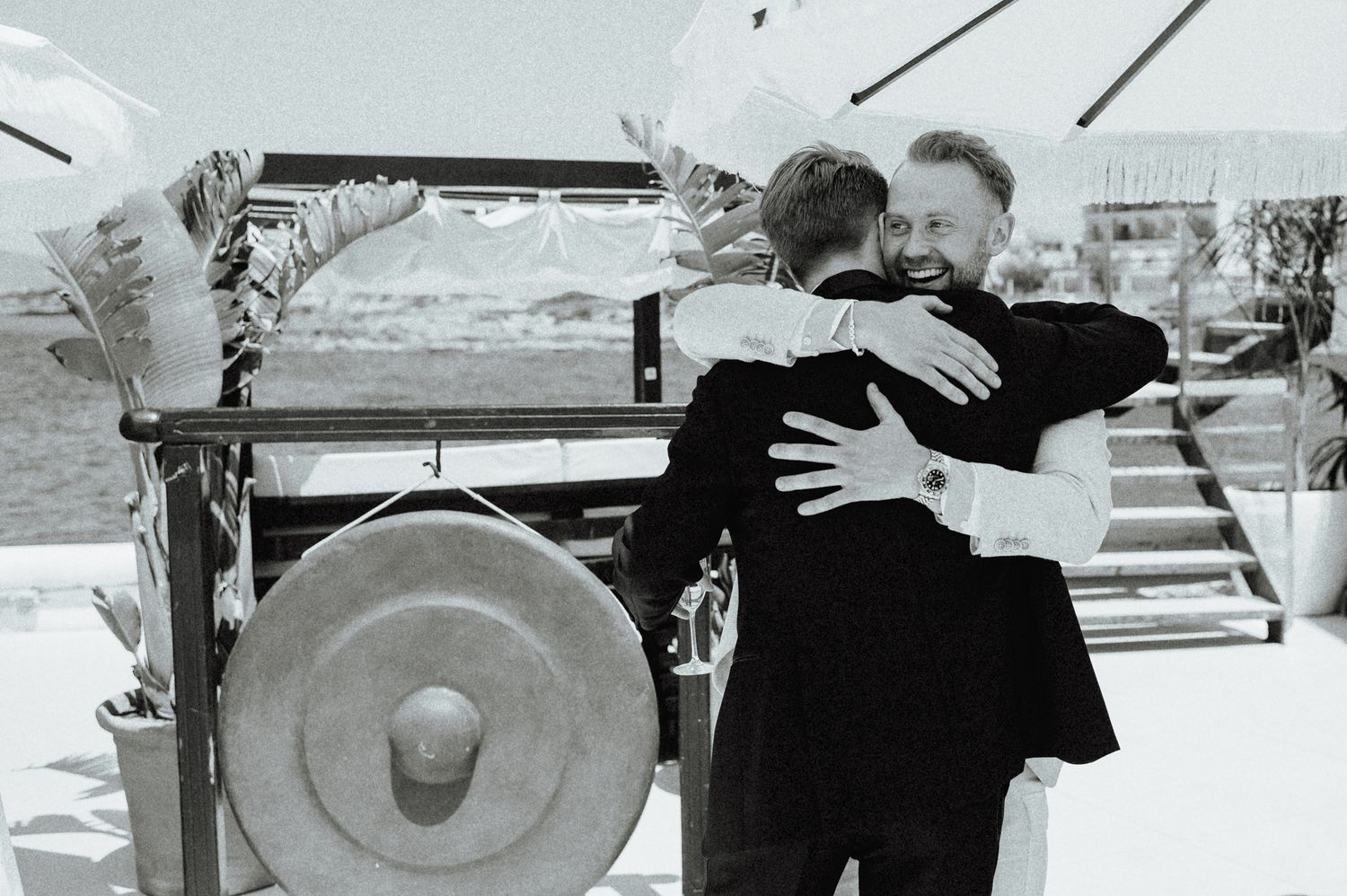 Two men sharing a warm embrace on a yacht deck during a wedding celebration.