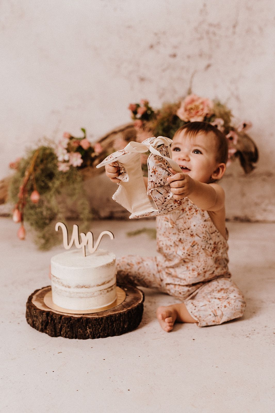 Baby girl in floral romper smashing her first birthday cake topped with \