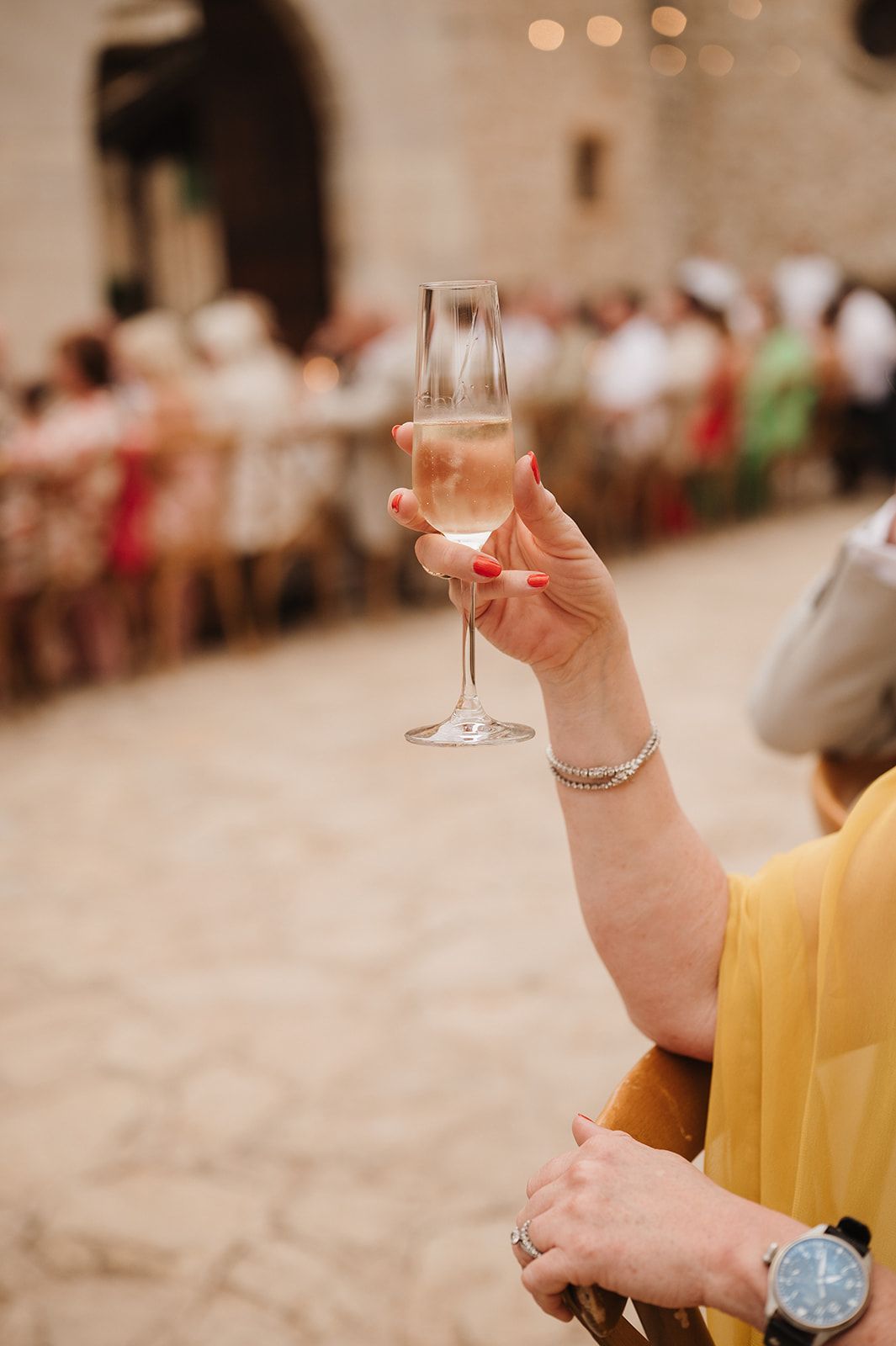 Hand with red nails raising a champagne flute during an outdoor wedding toast.