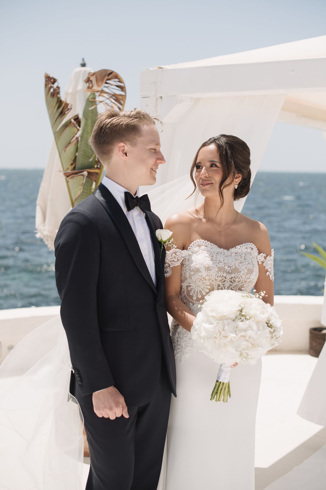 Bride and groom exchange vows at oceanfront wedding ceremony, bride holding white peony bouquet.