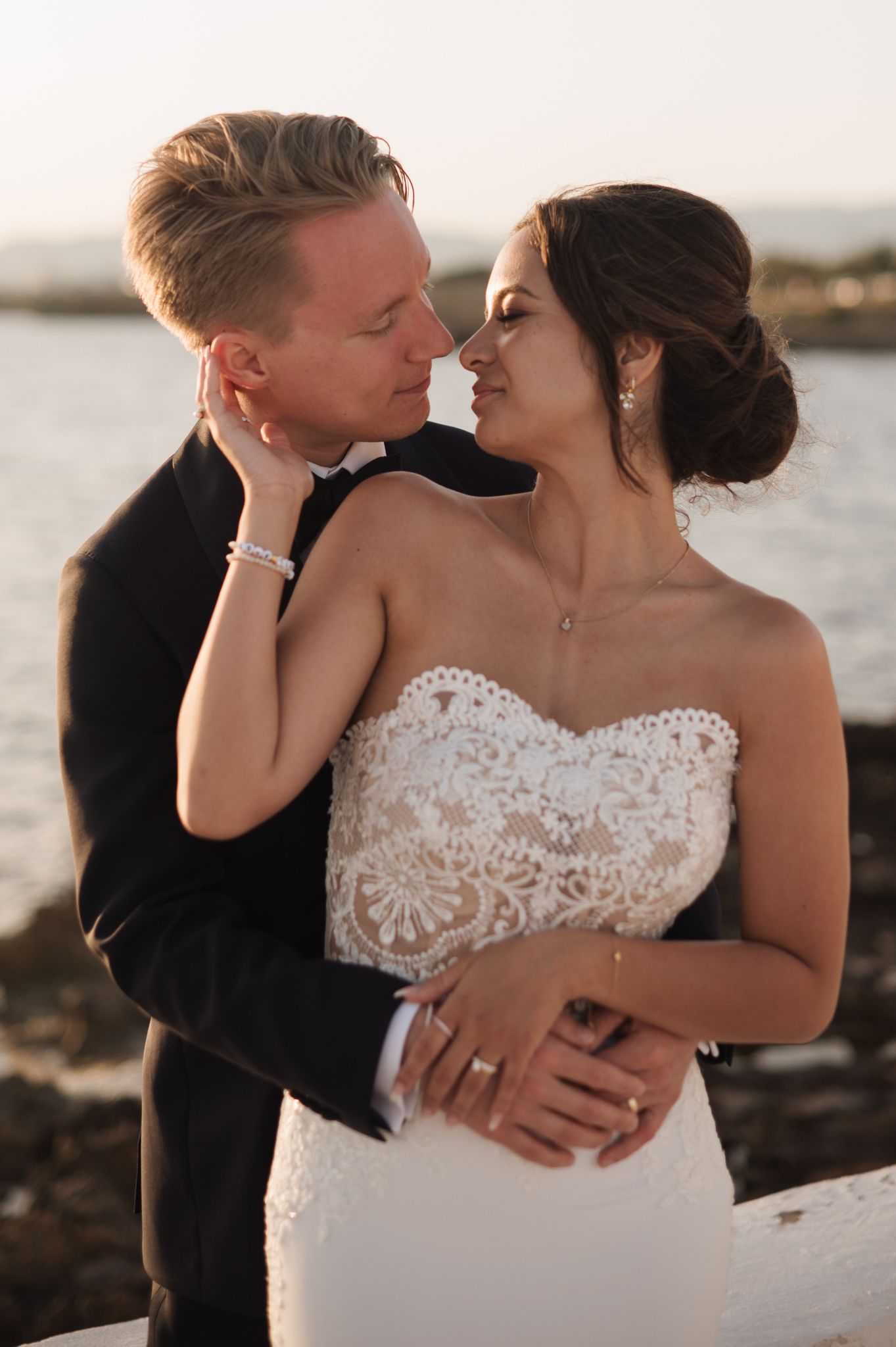 Bride and groom sharing an intimate moment in lace wedding dress at seaside golden hour.