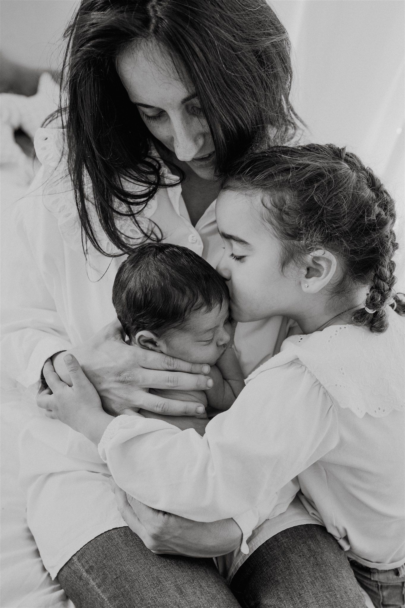 Black and white photo of a mother and young girl lovingly cradling a newborn baby together.
