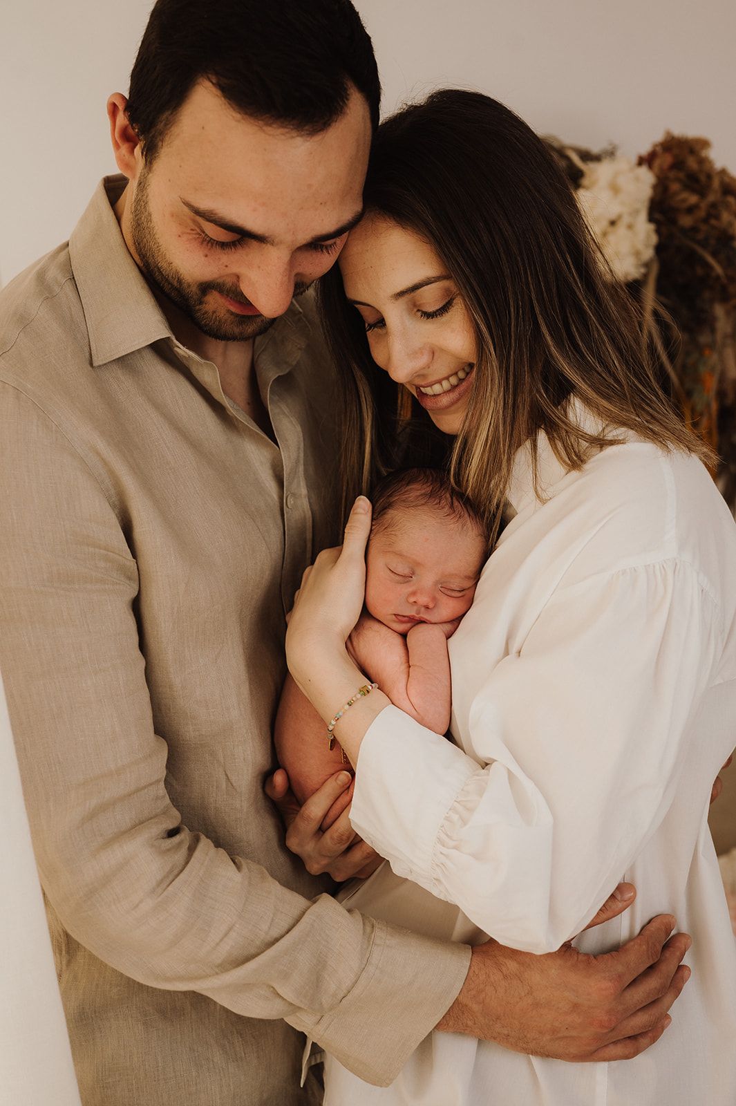 Happy parents smiling at their sleeping newborn baby together in a warm studio portrait.