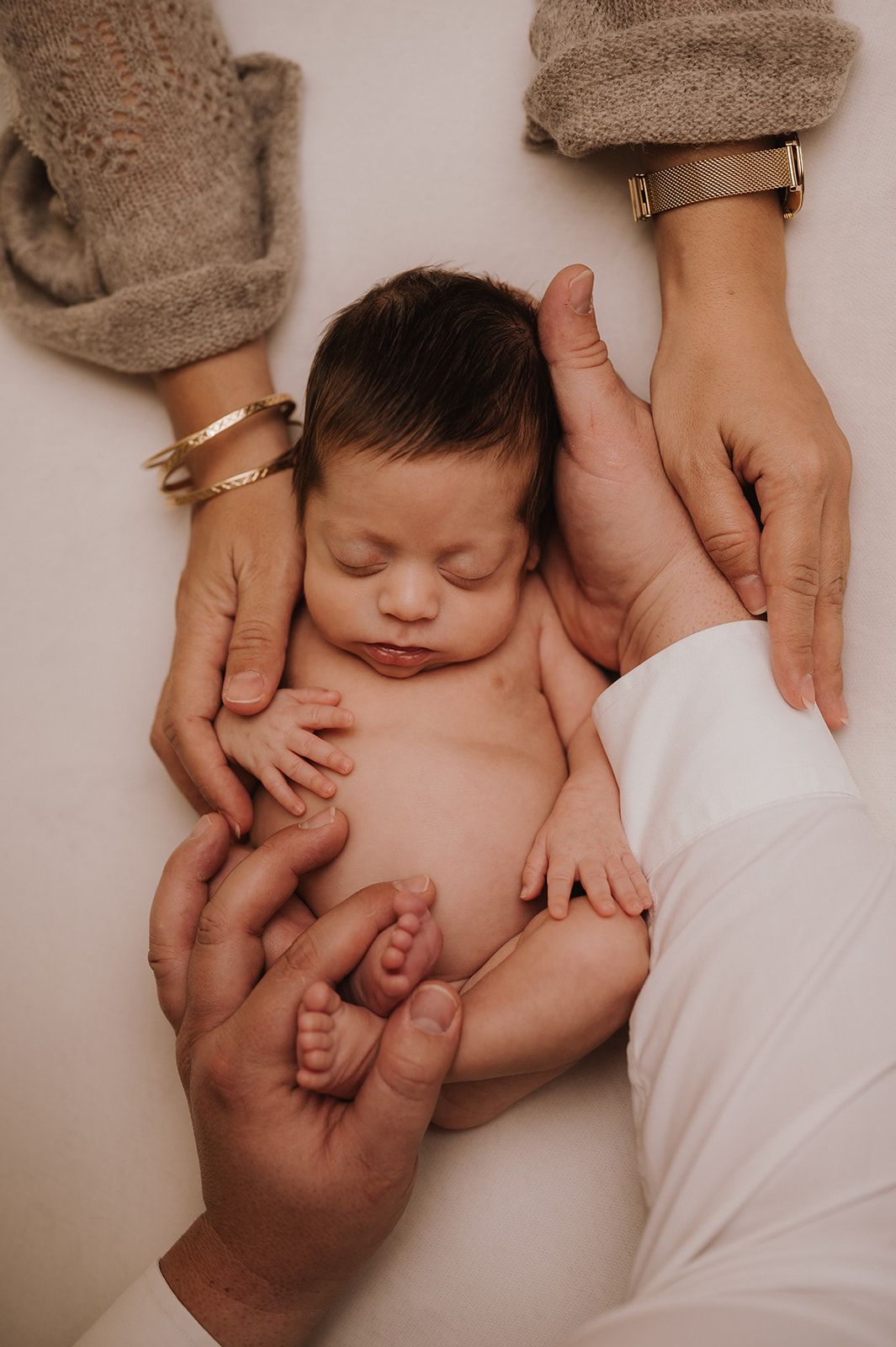 Sleeping newborn baby cradled by parents hands on white background.