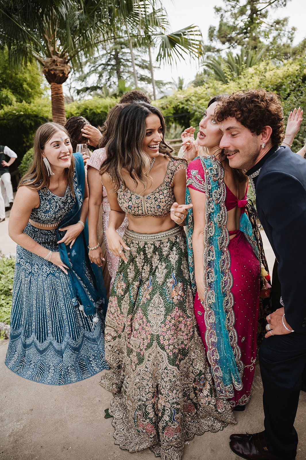 Guests celebrating in vibrant Indian lehengas at an outdoor wedding reception.