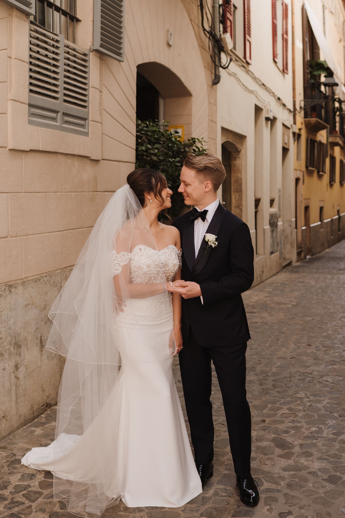 Bride and groom share a romantic moment on a cobblestone street, bride in lace mermaid gown.