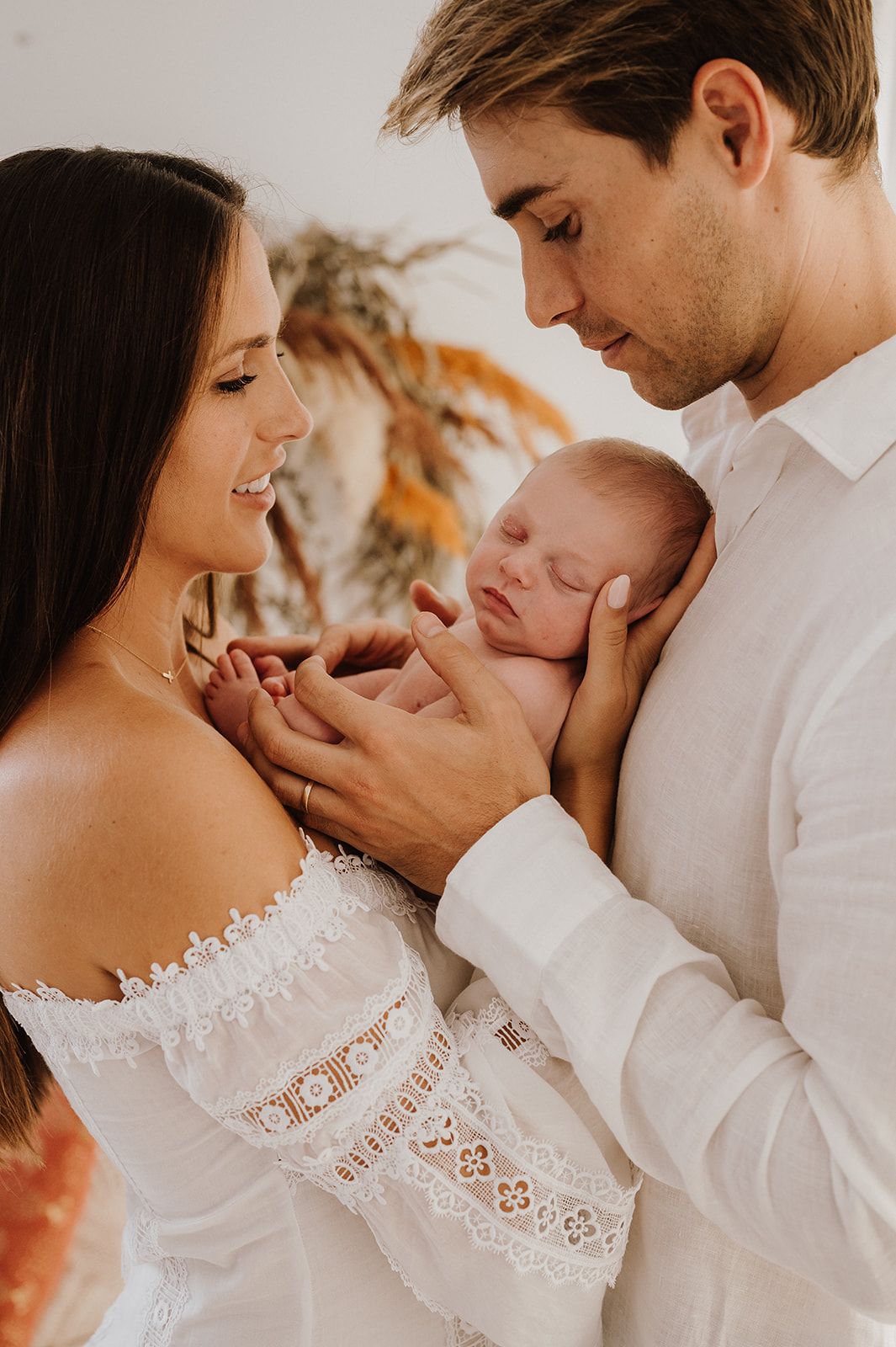 Young couple in white holding sleeping newborn baby in warm lifestyle portrait.