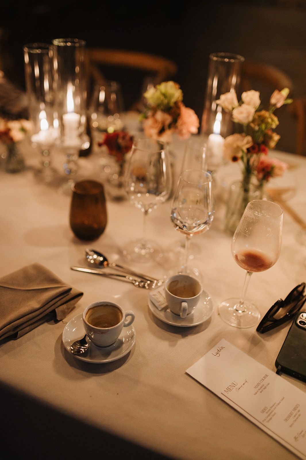 Elegant wedding table setting with espresso cups, wine glasses, candles, and floral arrangements.