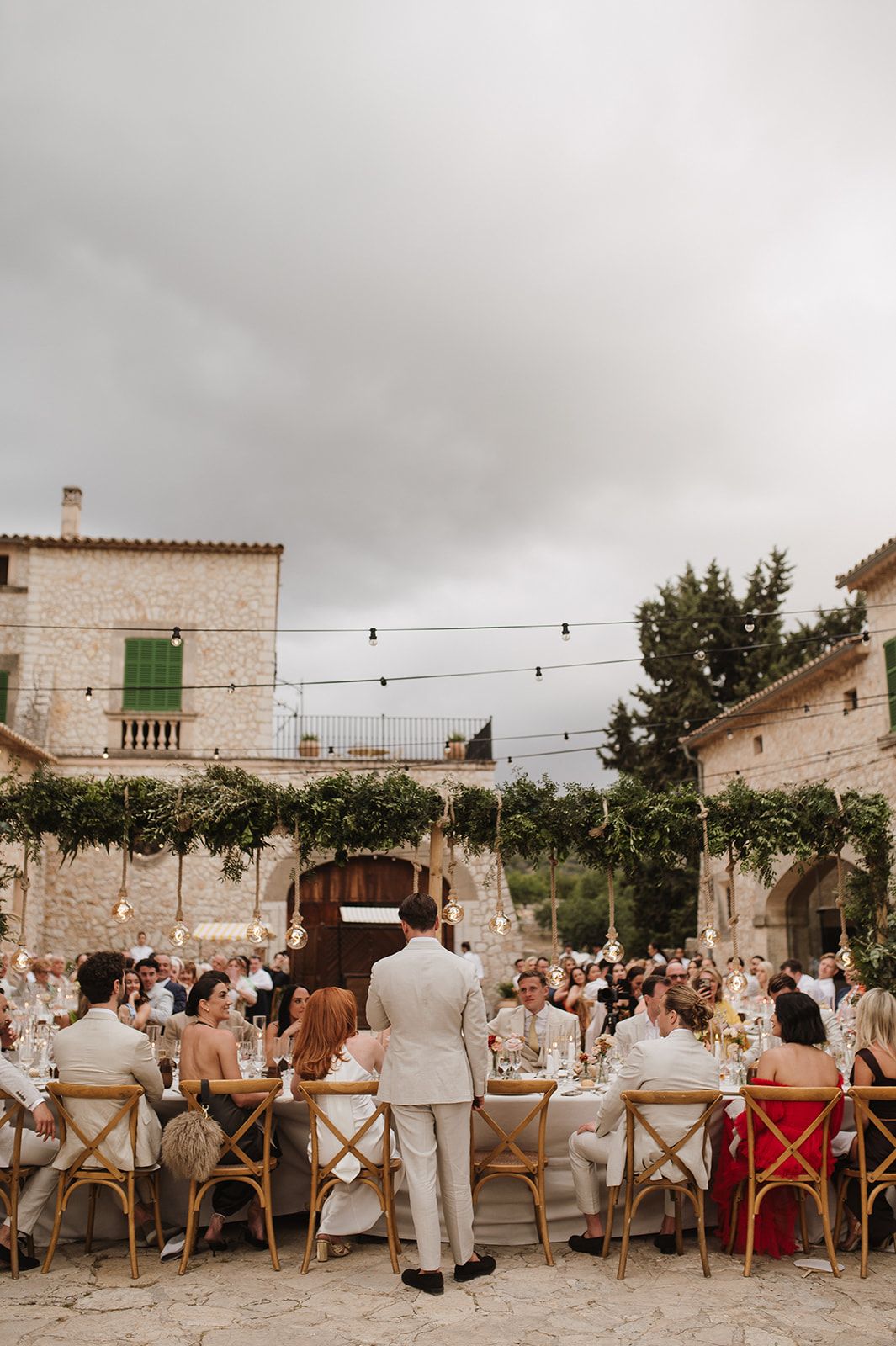 Outdoor wedding reception in a rustic stone courtyard with string lights and lush greenery overhead.