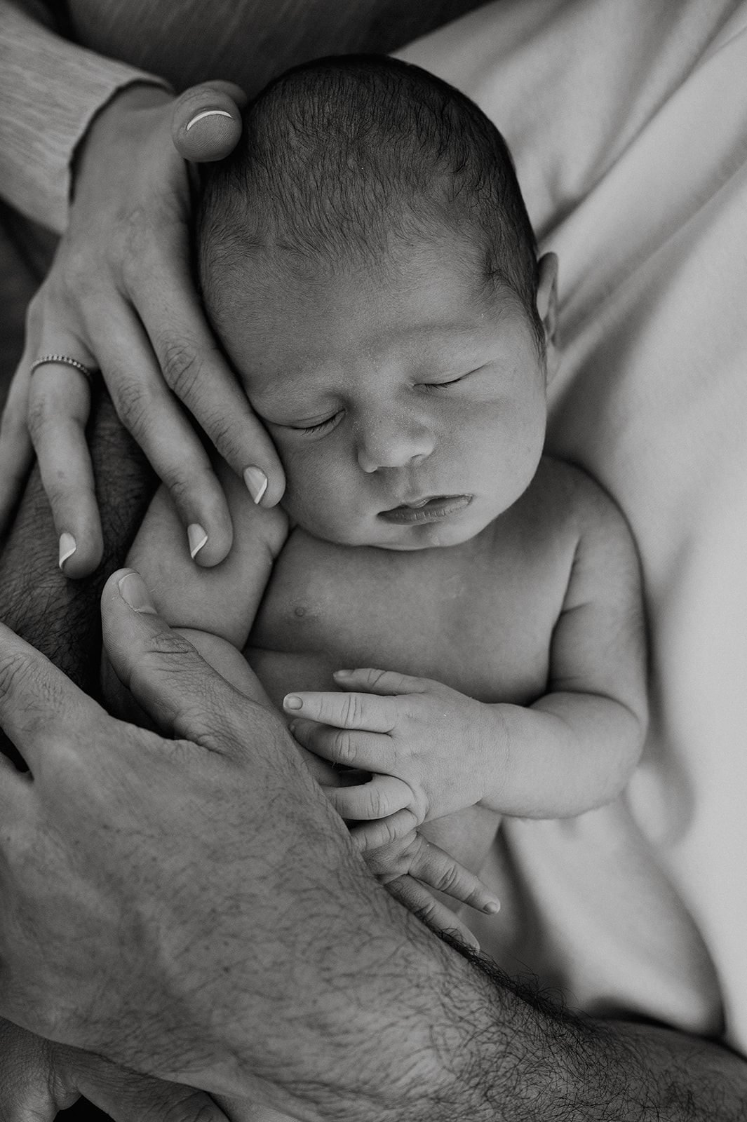 Black and white photo of a sleeping newborn baby cradled gently in parents hands.