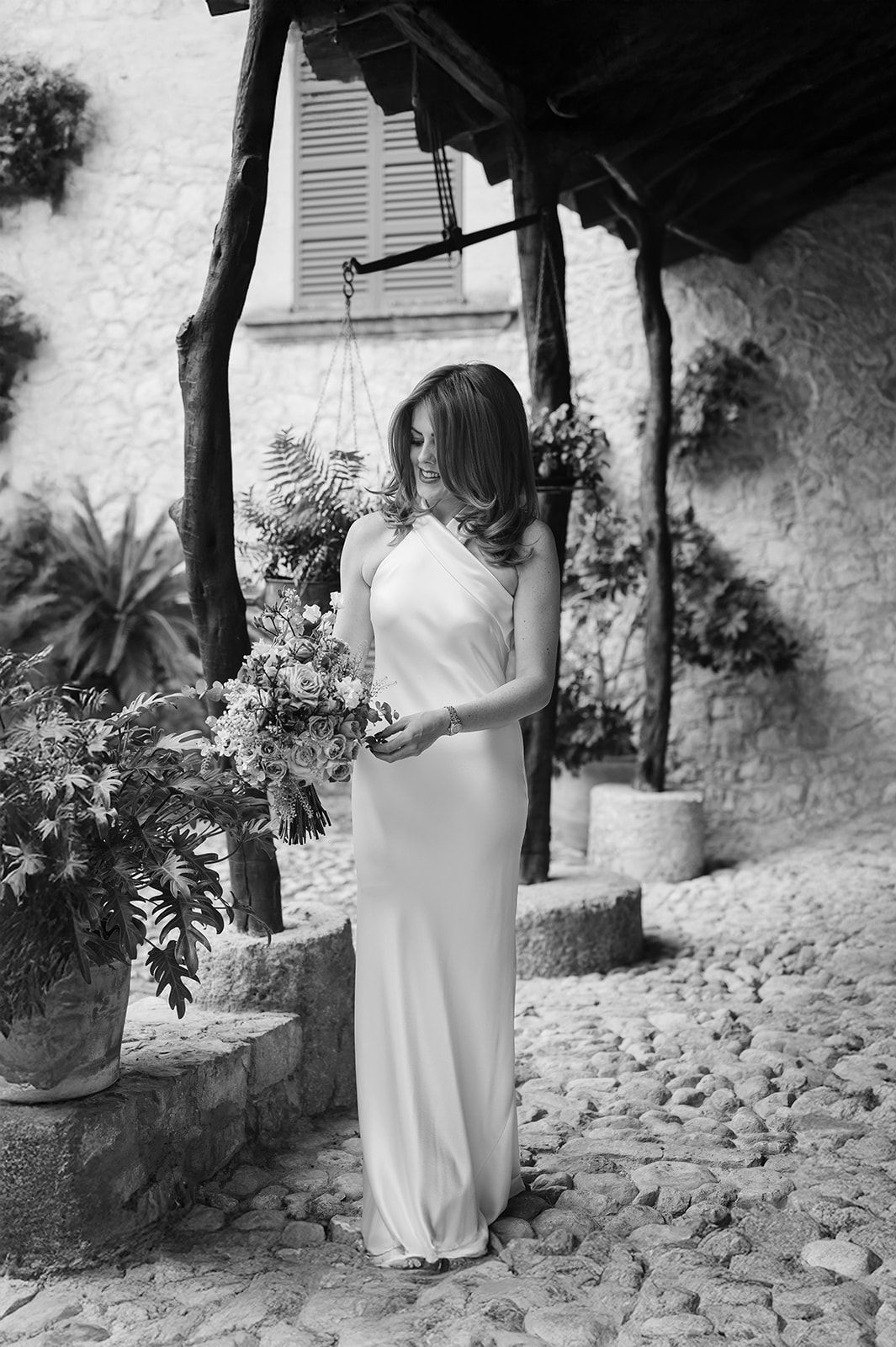 Black and white photo of a bride holding a floral bouquet in a cobblestone courtyard.