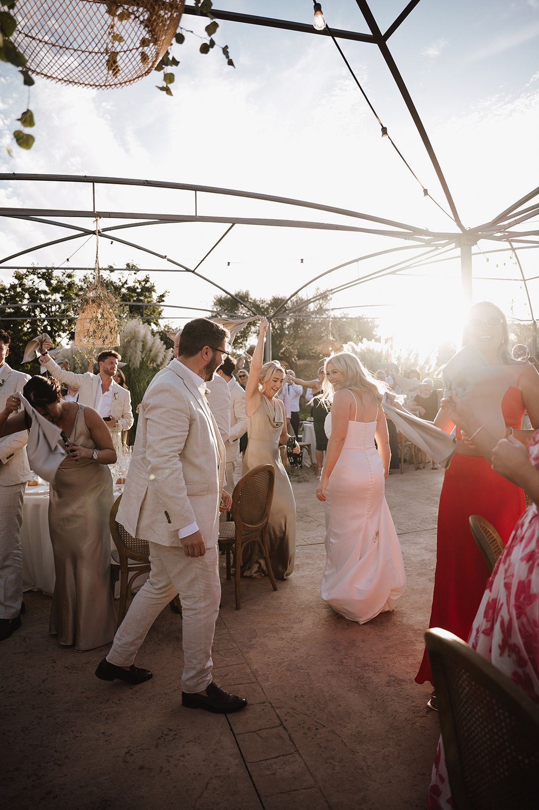 Bride and groom make grand entrance at outdoor wedding reception bathed in golden sunset light.