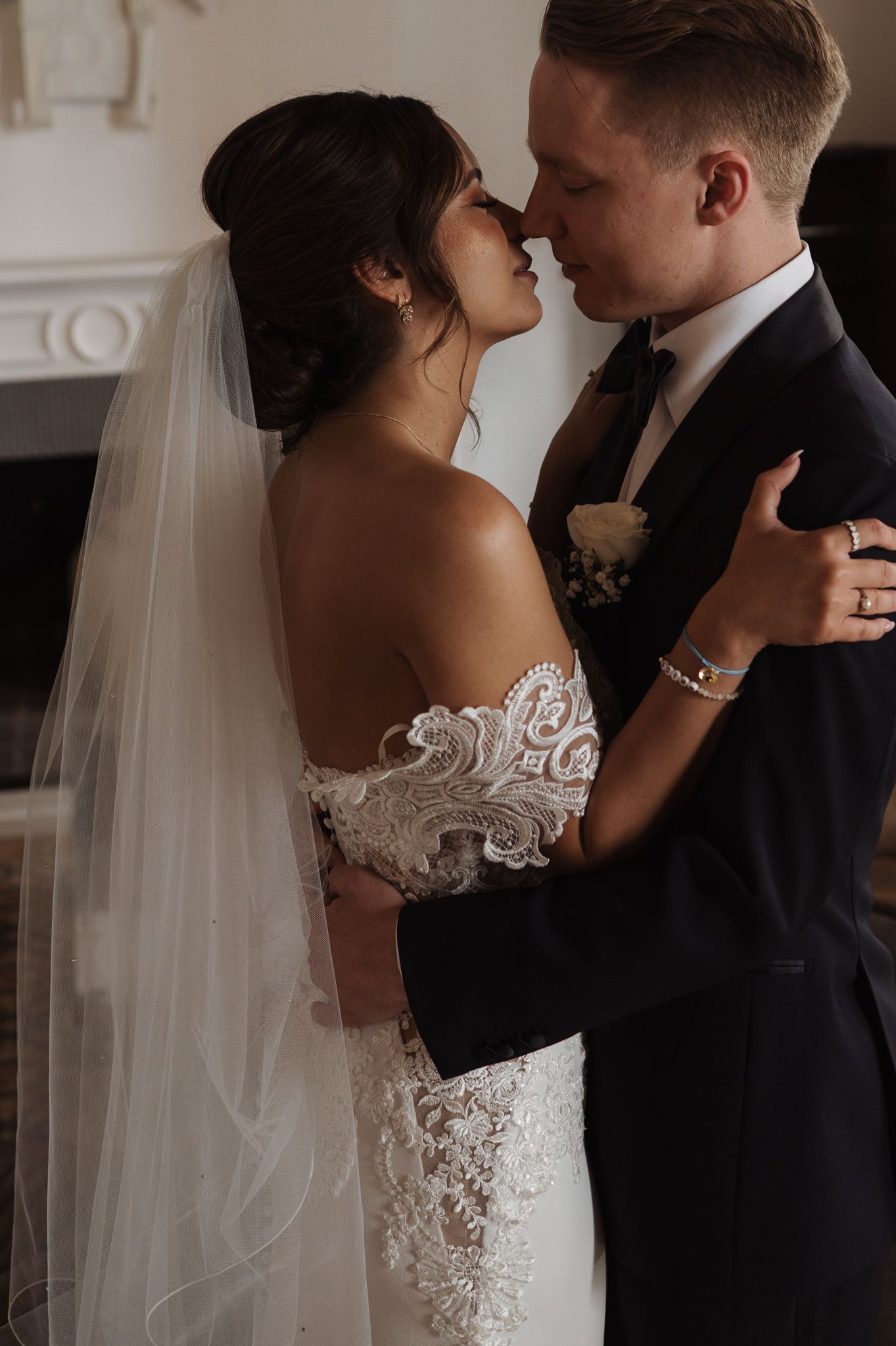 Bride and groom sharing a romantic moment in close embrace, bride wearing off-shoulder lace wedding dress with veil.