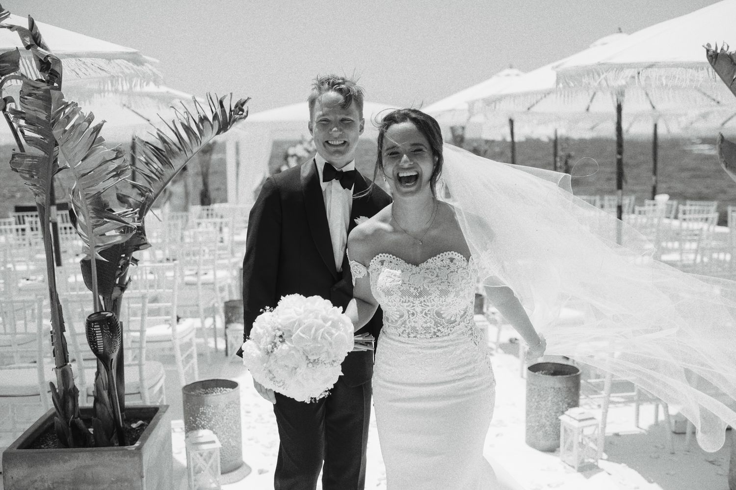 Happy bride and groom pose together after their outdoor wedding ceremony, bride holding white bouquet.