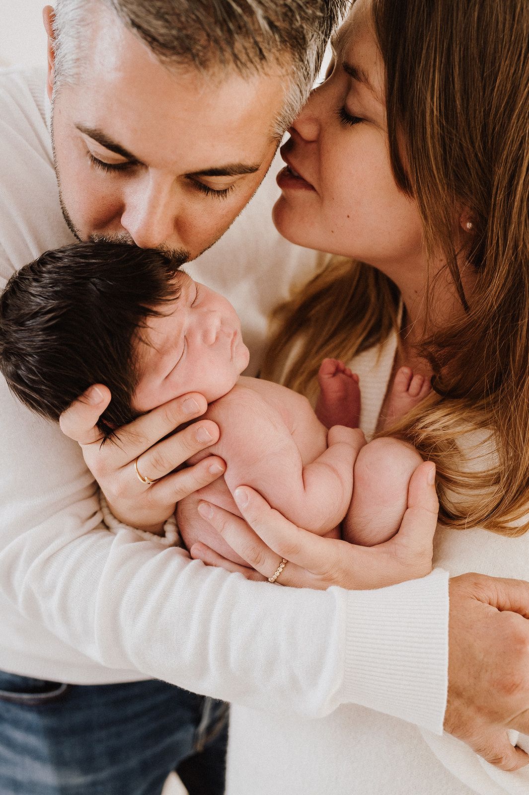 Parents kissing their newborn baby together, sharing a tender family moment of love and joy.