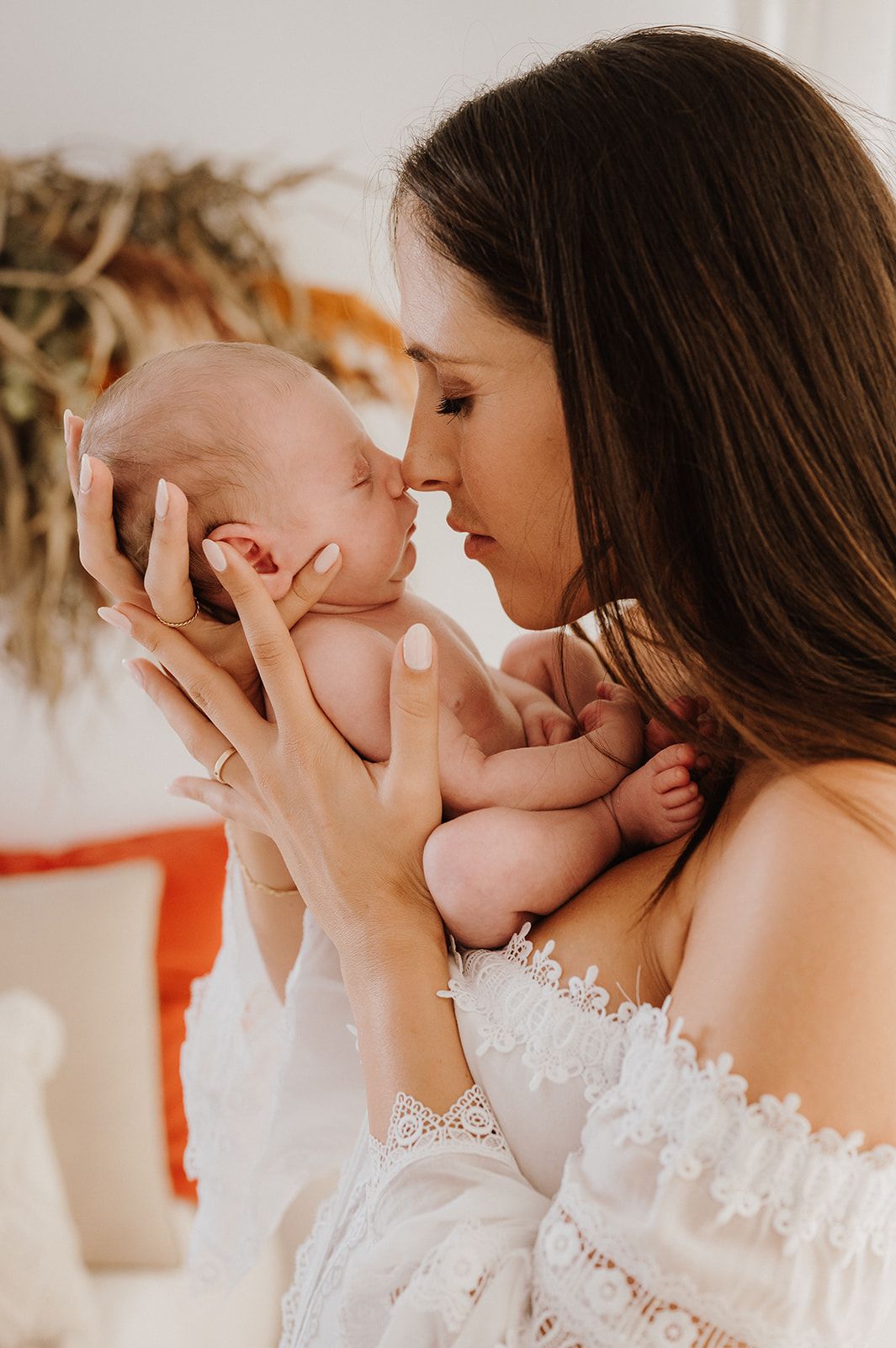 Loving mother in white dress holding and nuzzling her newborn baby tenderly.