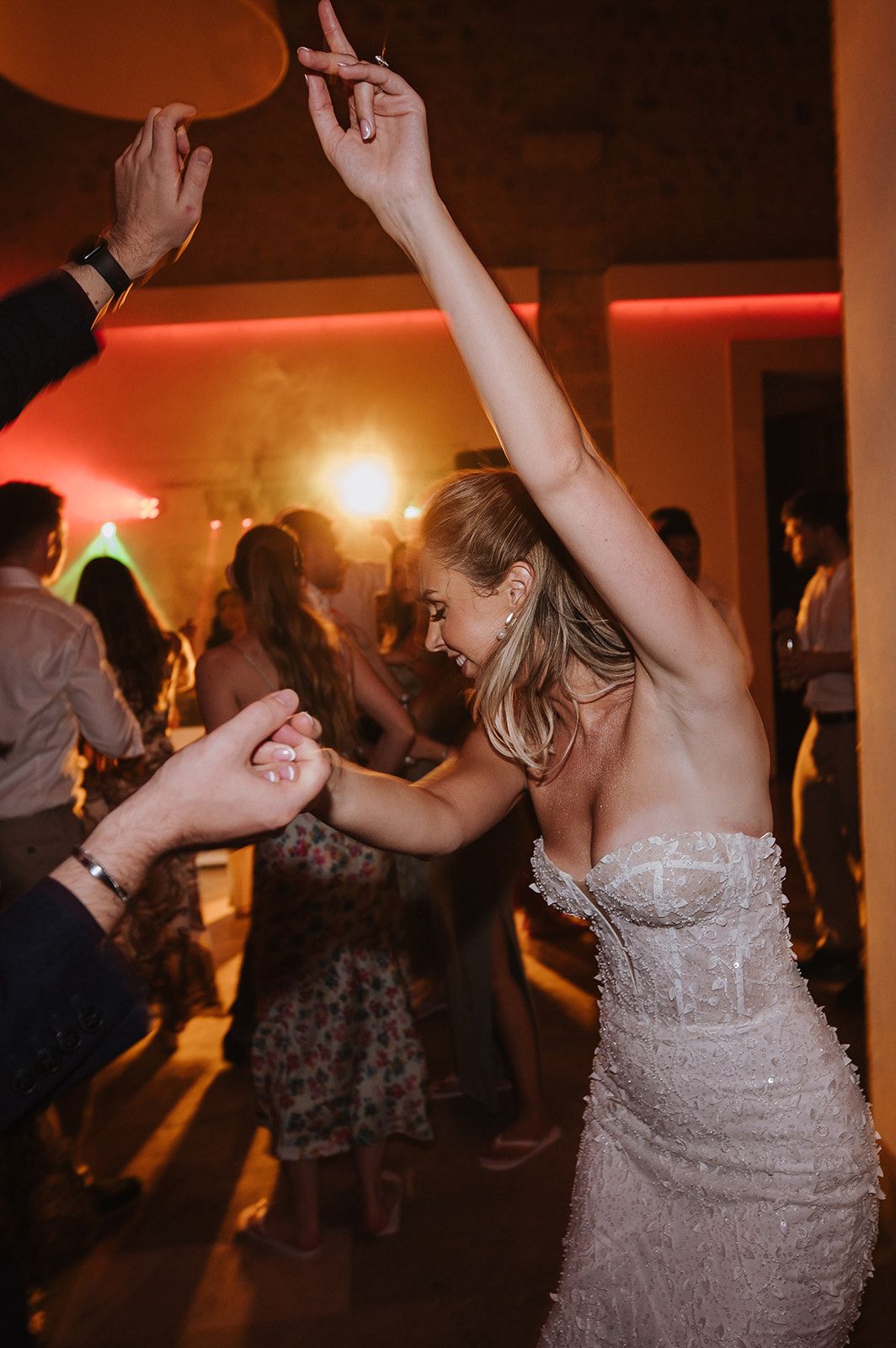 Bride in a beaded strapless gown dancing joyfully at a wedding reception with arm raised.