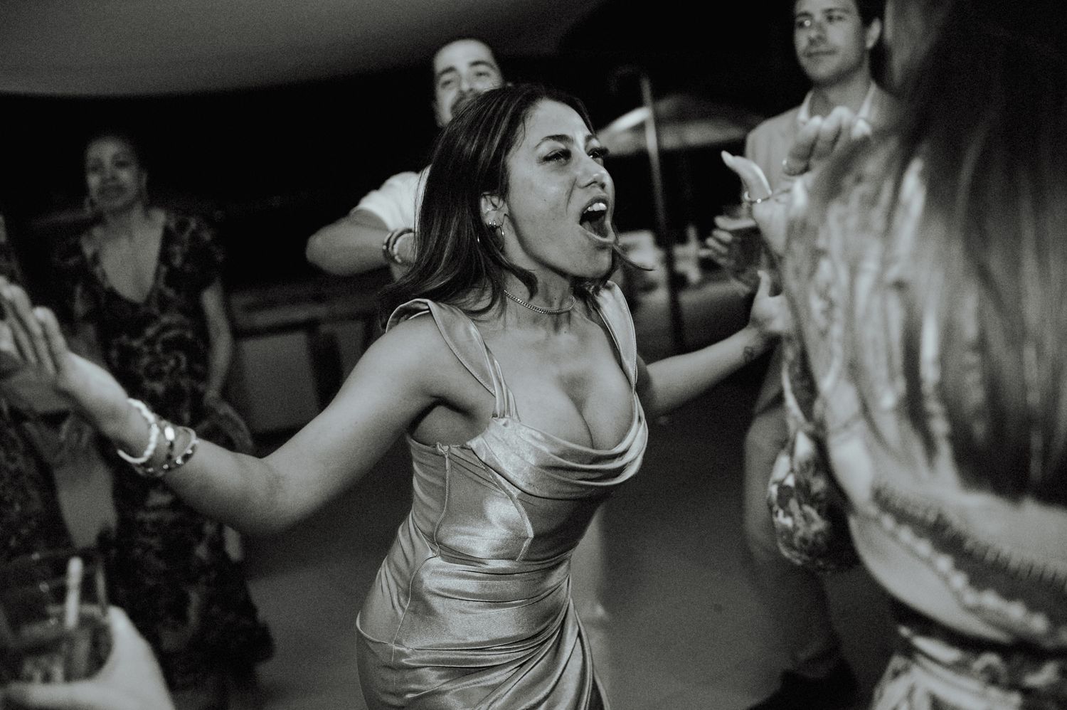 Woman in gold dress dances joyfully at lively wedding reception in black and white photo.