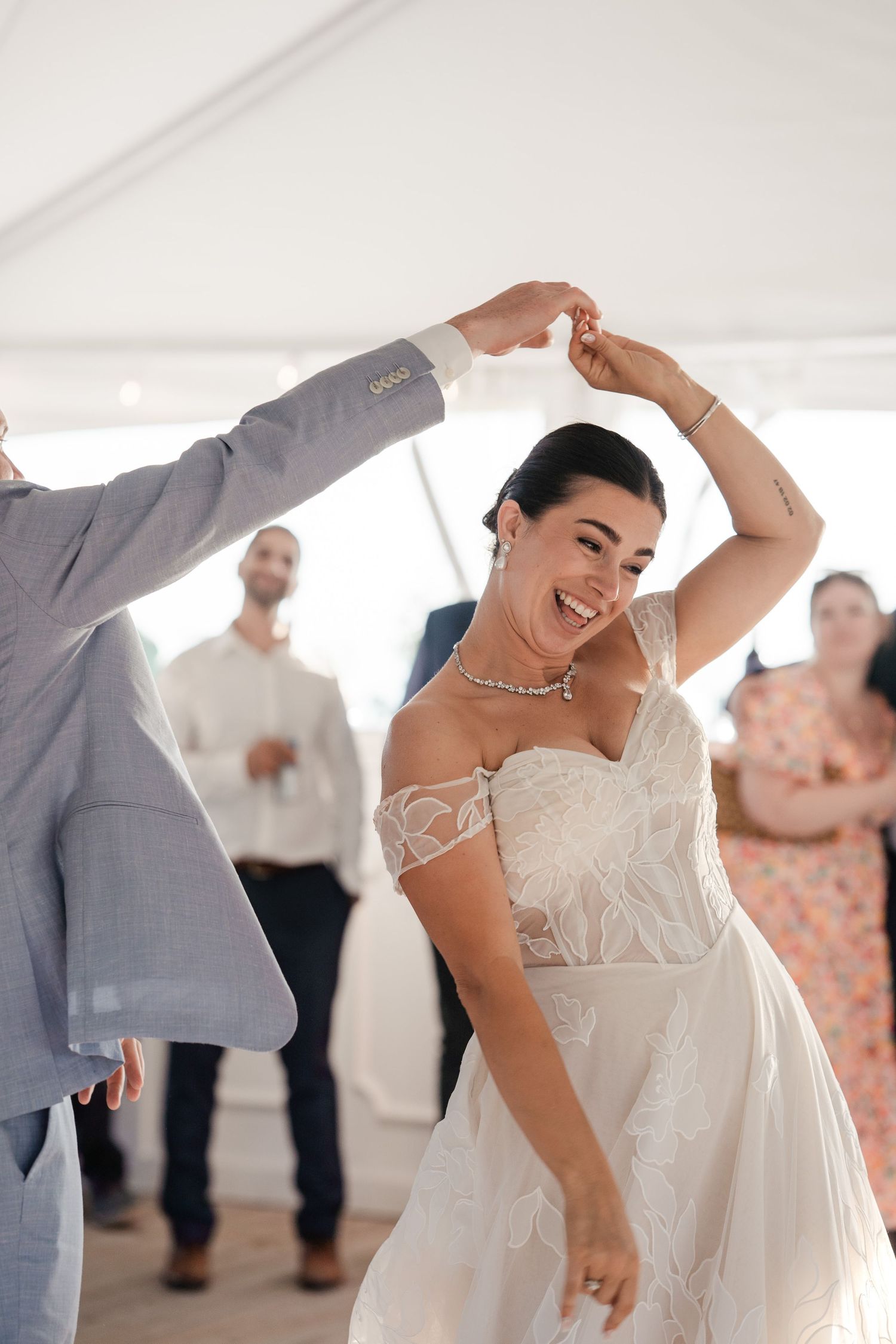 Joyful bride in a lace off-shoulder gown being twirled by the groom during their first dance.