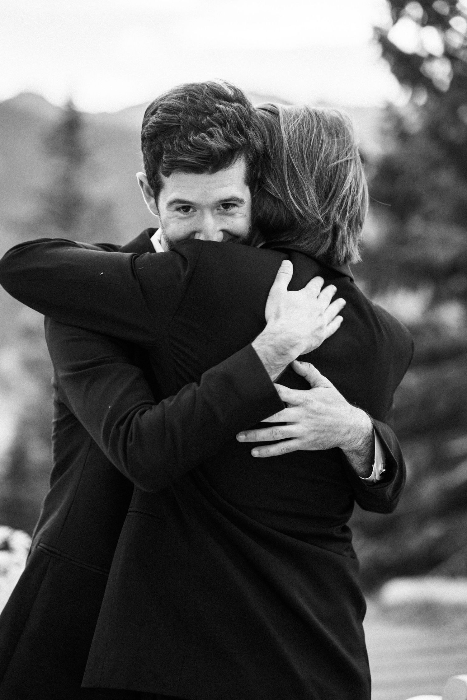 A man and woman share an emotional embrace outdoors in a black and white wedding photo.