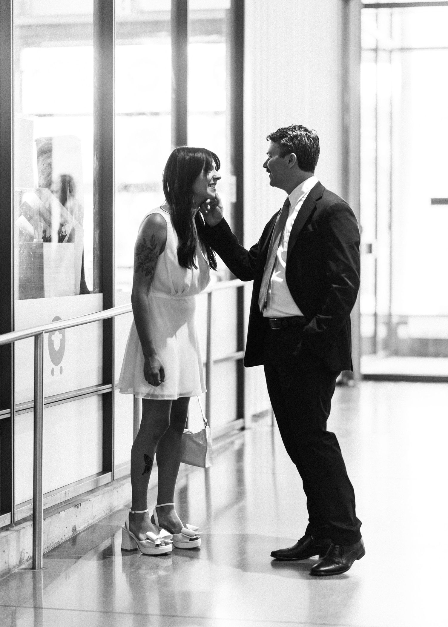 Black and white photo of a couple sharing an intimate moment in a bright modern building lobby.
