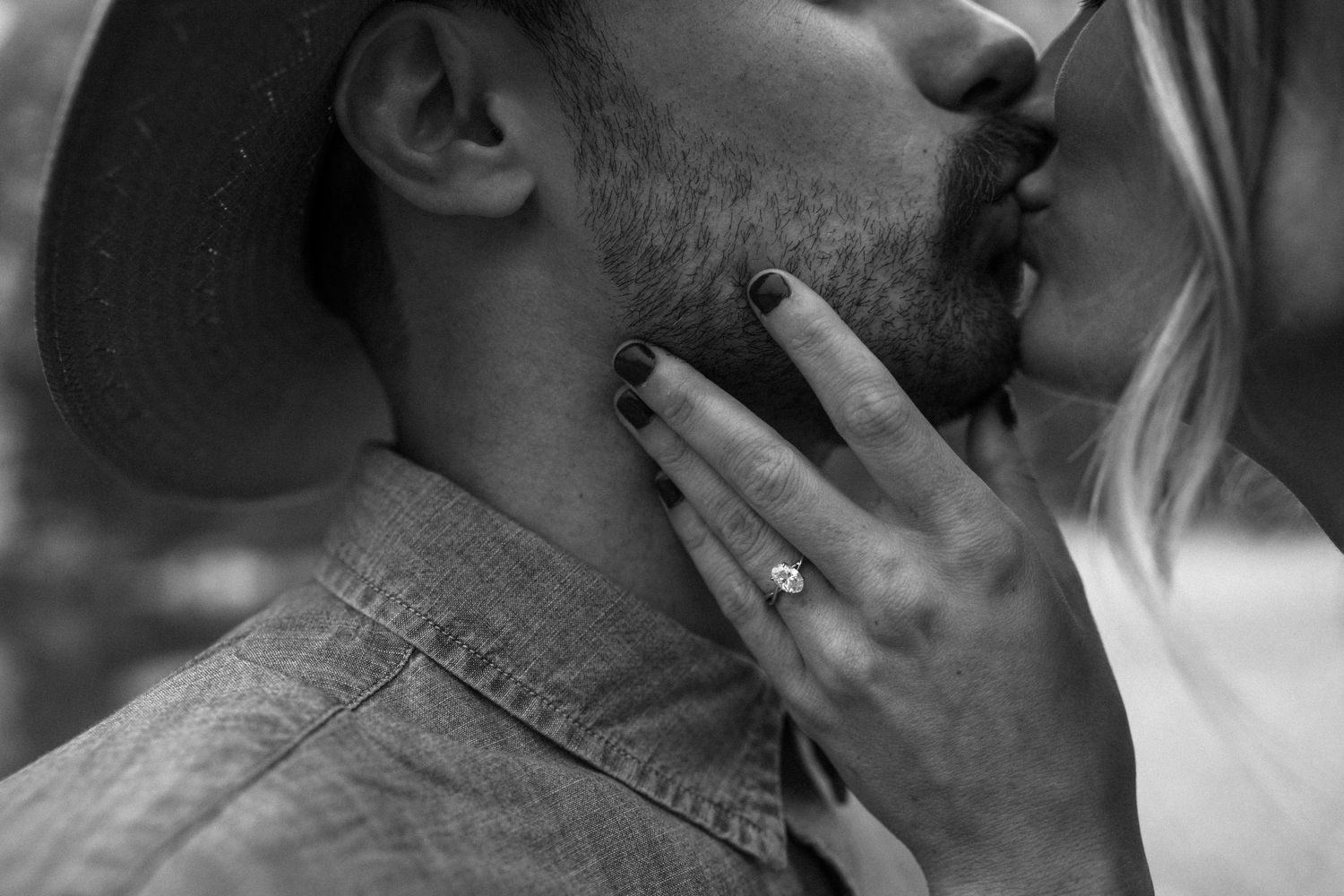 Black and white close-up of couple kissing, showing diamond engagement ring on brides hand.