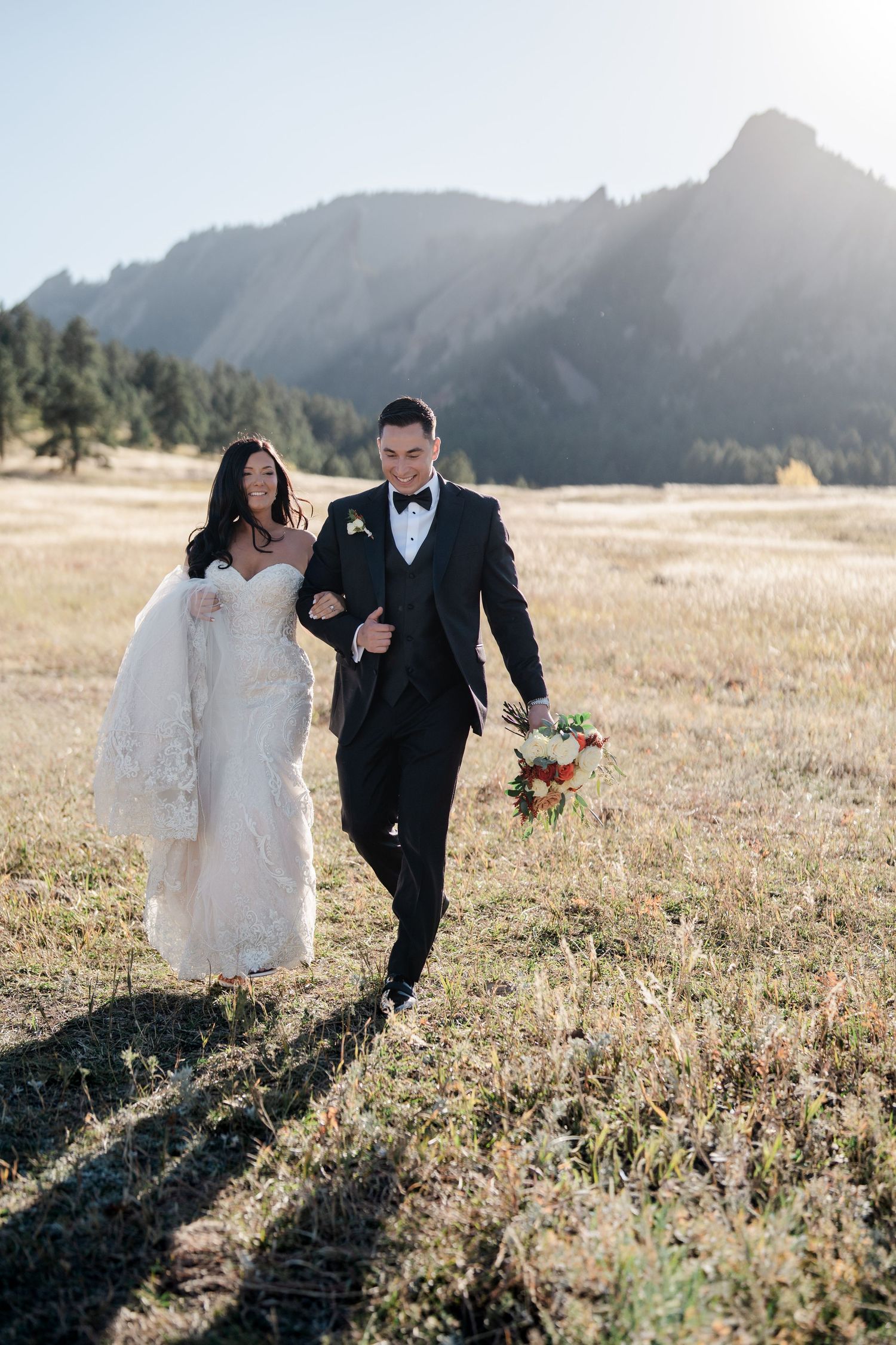 Bride and groom walking through golden meadow with iconic Boulder Flatirons mountain backdrop.