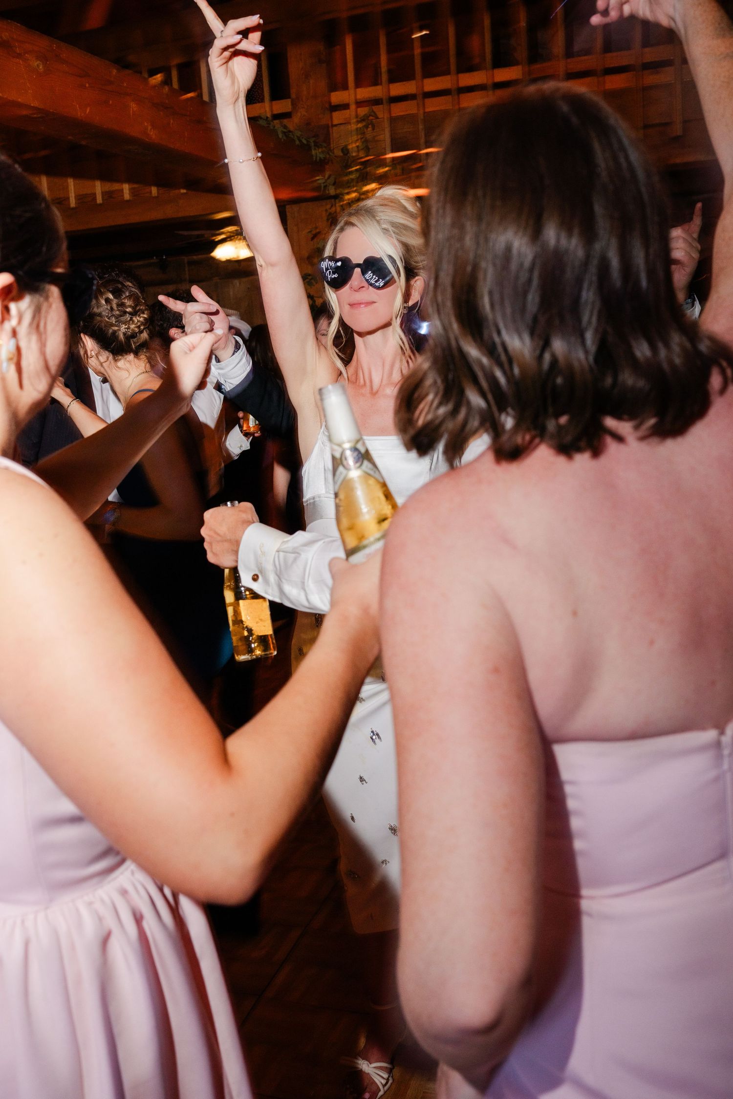 Bride dancing with sunglasses and champagne bottle at wedding reception.