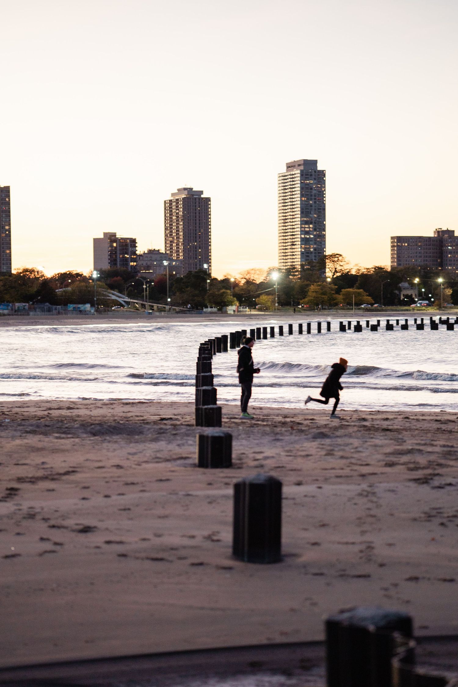 Silhouette of couple playing on sandy Chicago lakefront beach at sunset with city skyline in background.