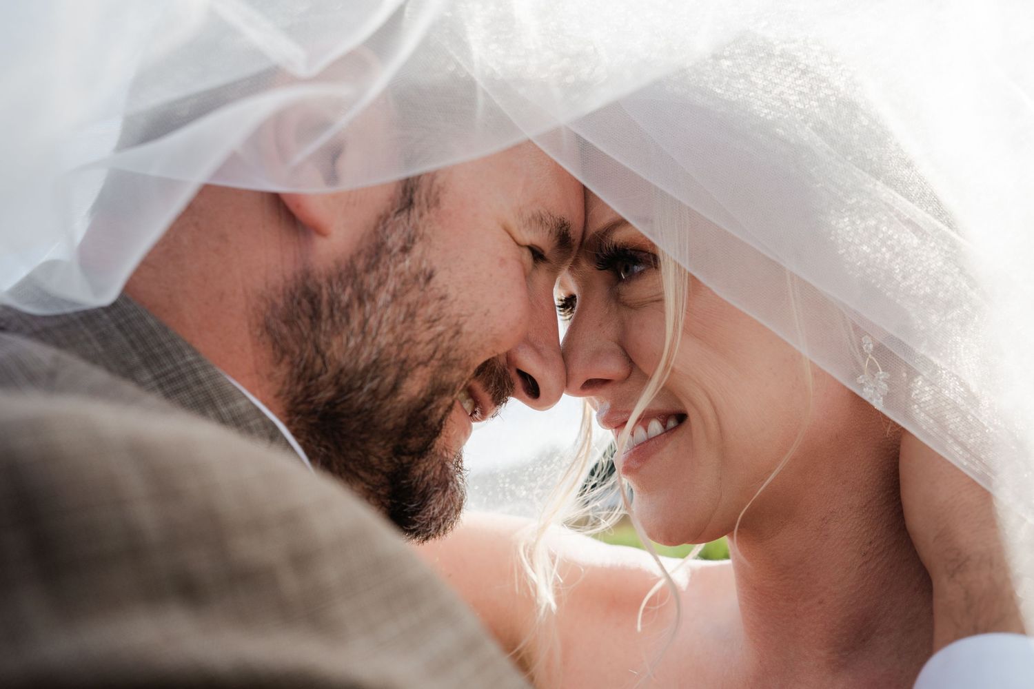 Intimate close-up of bride and groom touching foreheads under flowing wedding veil.