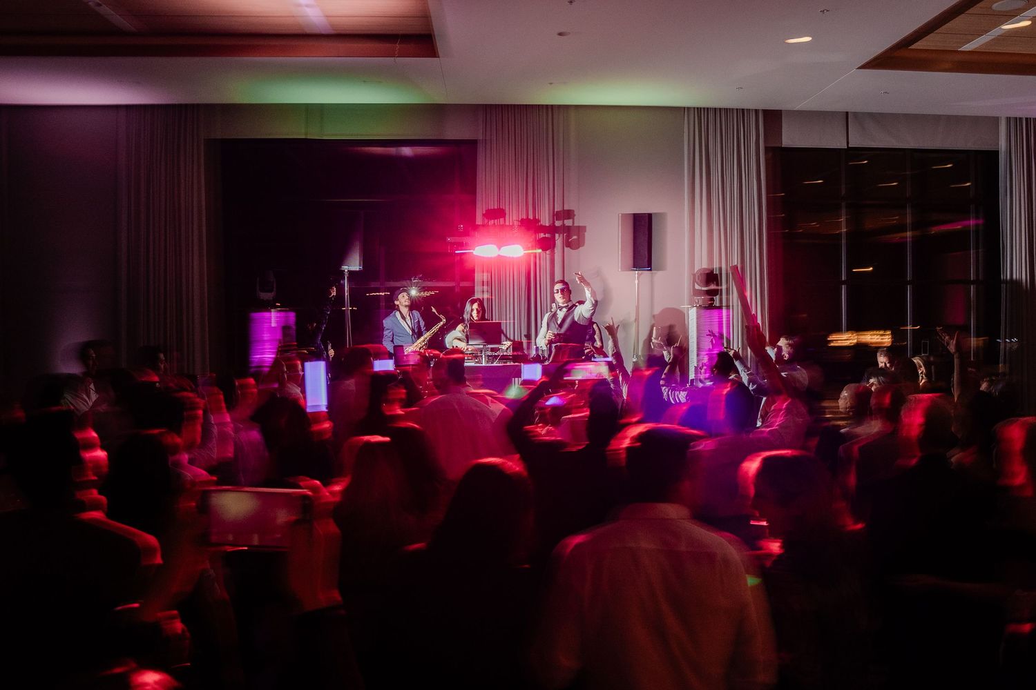 Live band performing on stage at a wedding reception with guests dancing in pink lighting.