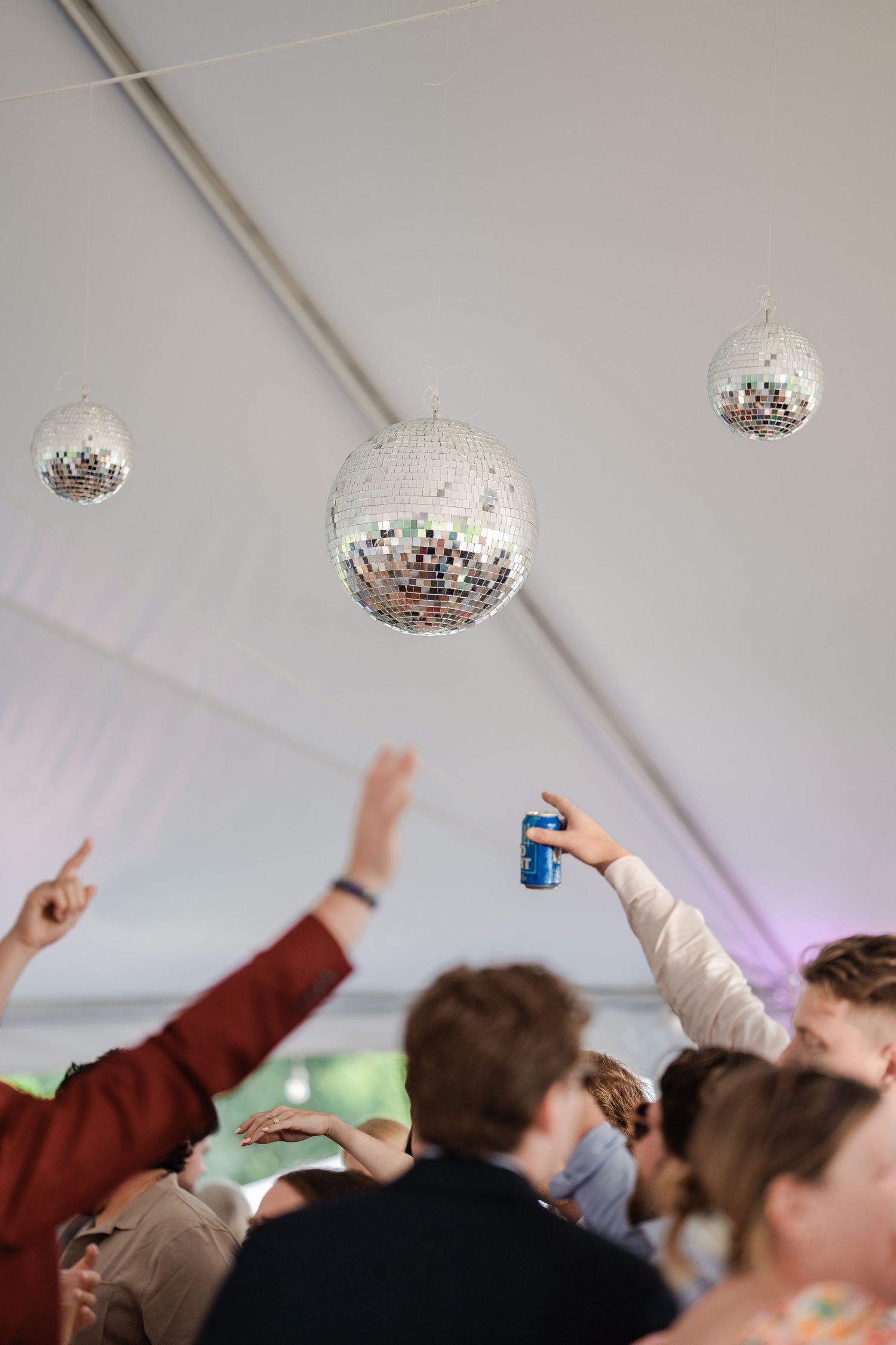 Disco balls hang above energetic wedding guests dancing under a white tent.