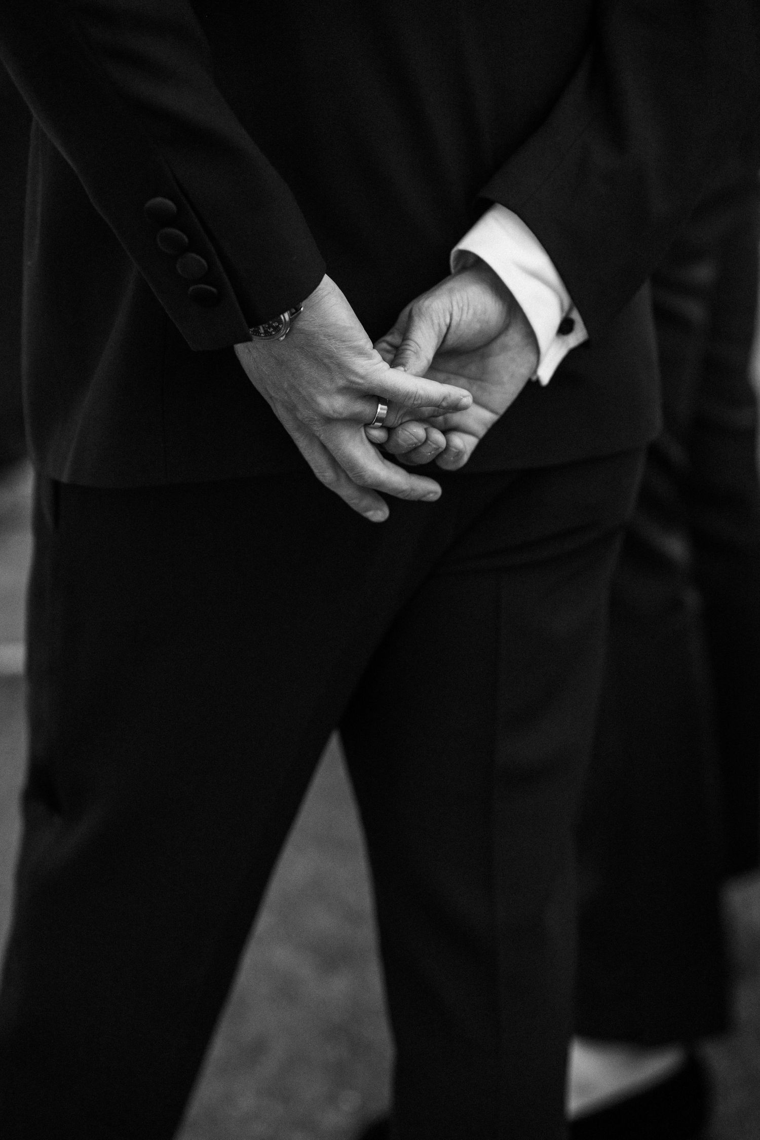 Close-up black and white photo of a groom clasping his hands nervously before a wedding ceremony.