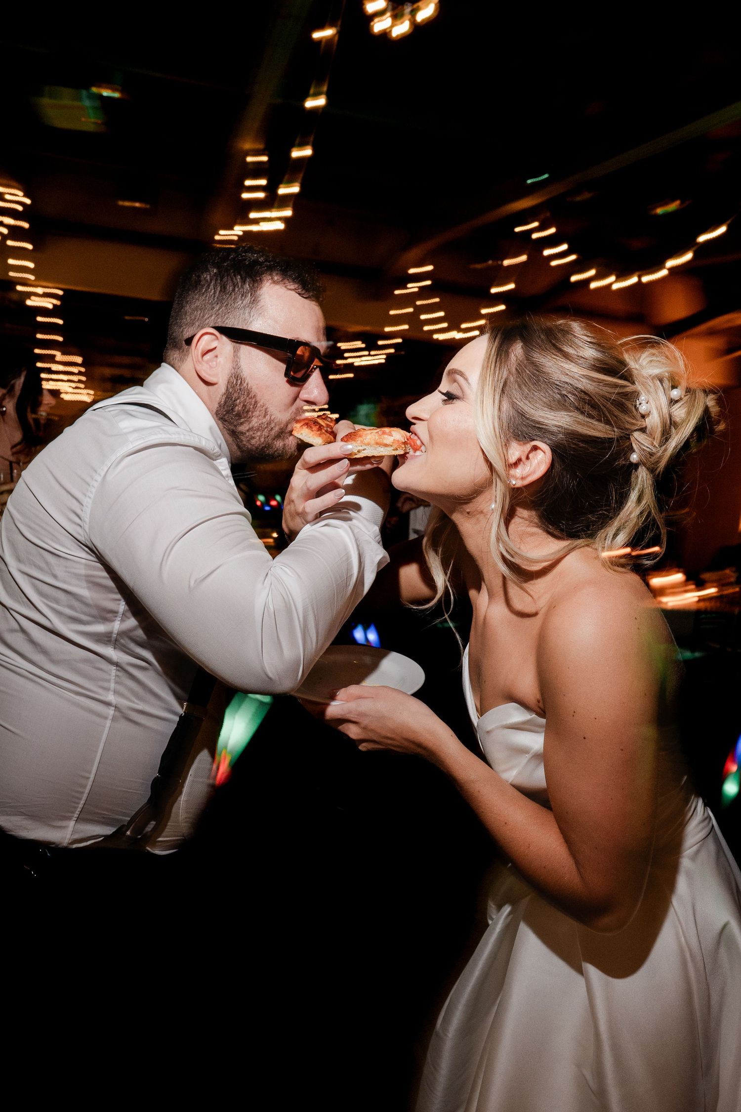 Bride and groom sharing a slice of pizza on the dance floor at their wedding reception.