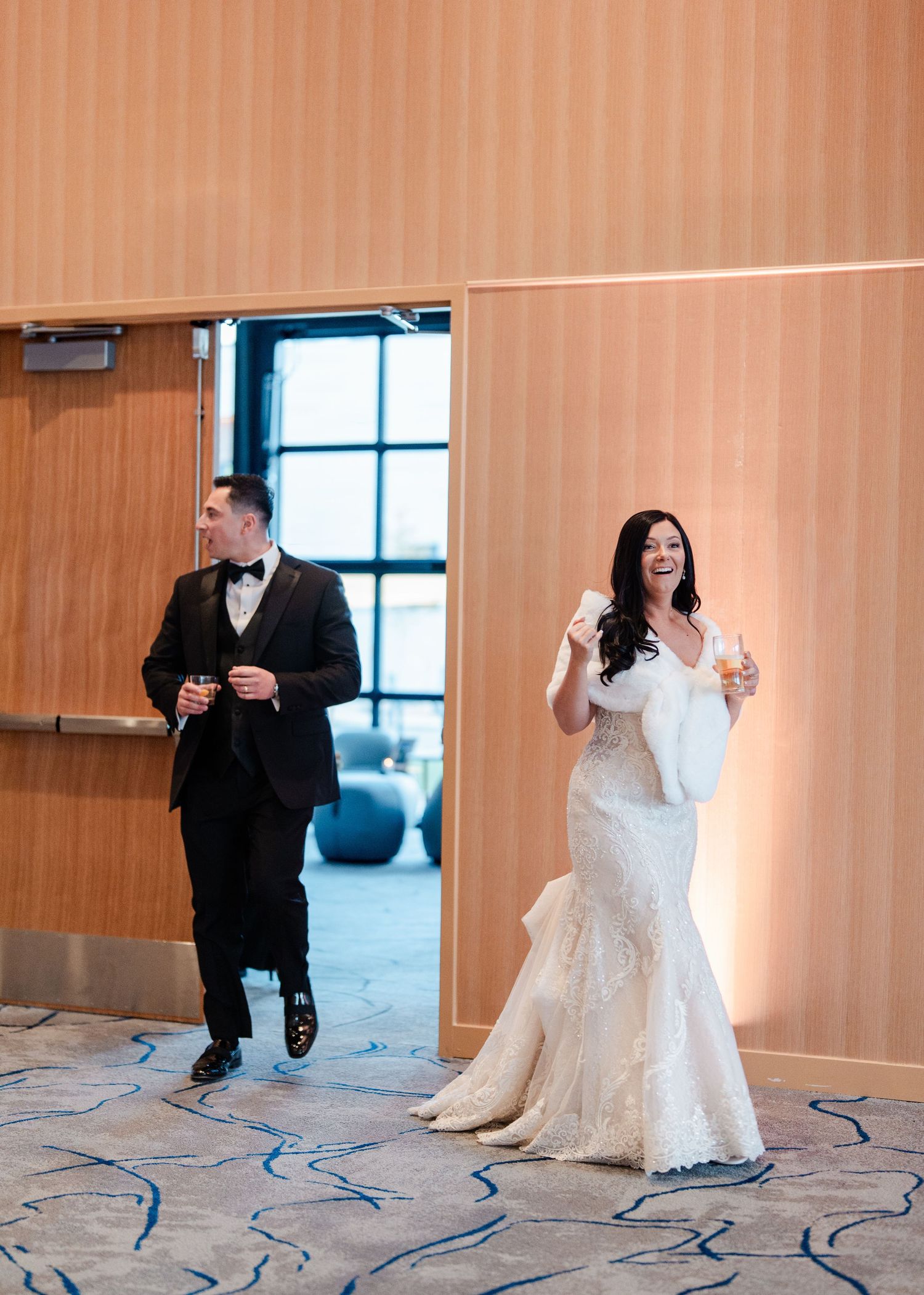 Bride in lace mermaid gown and groom in tuxedo making grand entrance at wedding reception.