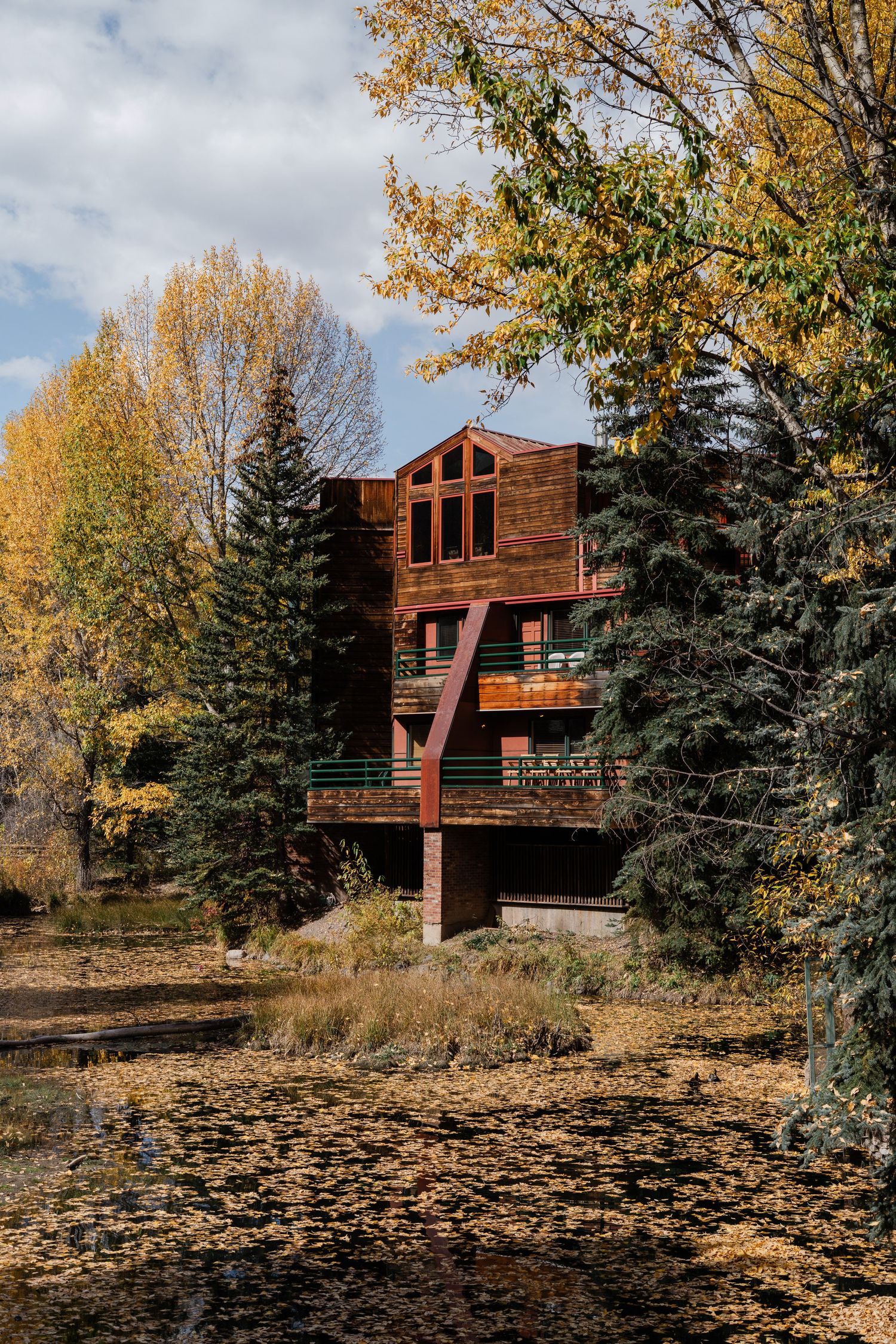 Rustic wooden lodge surrounded by colorful autumn trees reflected in a tranquil pond below.