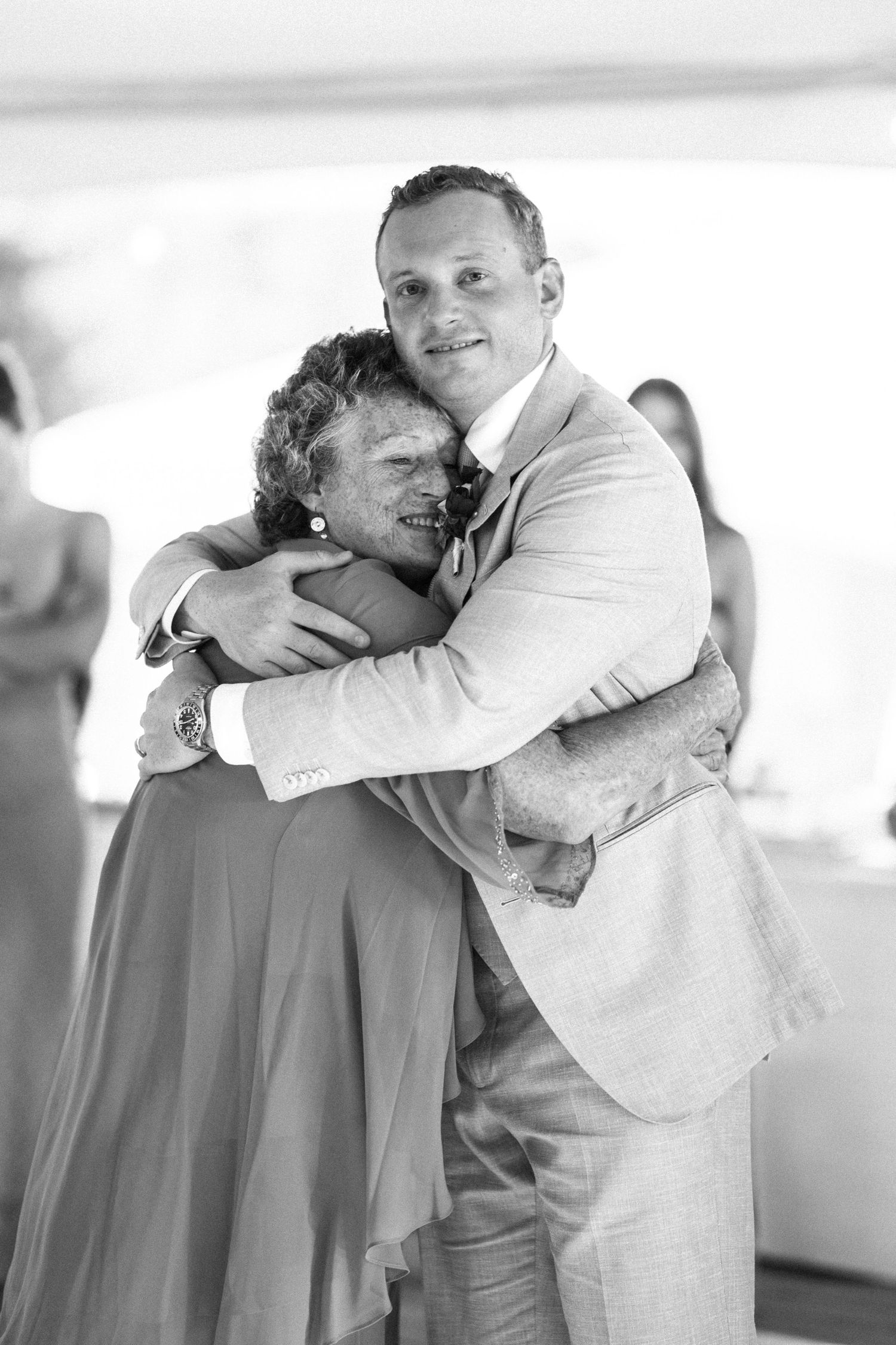 A groom in a suit shares an emotional hug with a woman during a wedding reception.