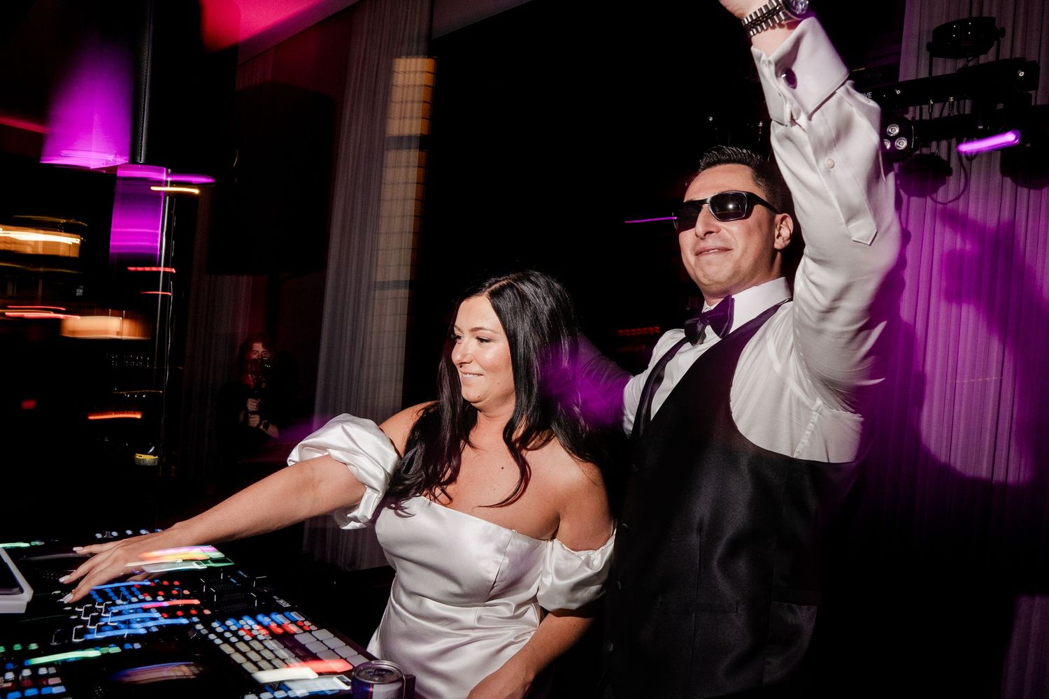 Bride and DJ celebrating together at a vibrant wedding reception with colorful lights.