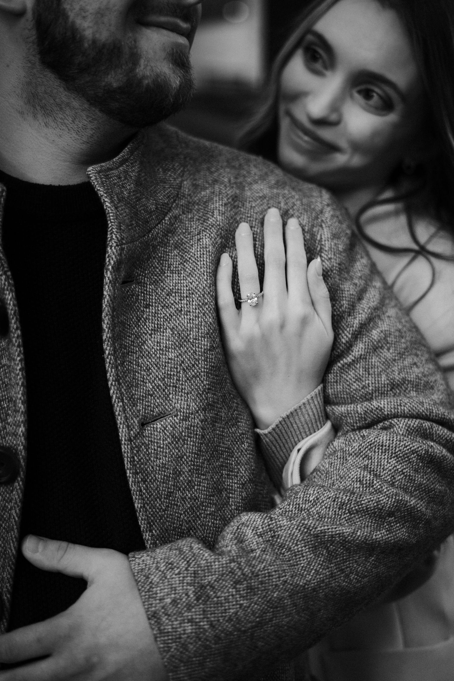 Close-up black and white photo of an engaged couple, woman displaying her diamond engagement ring.