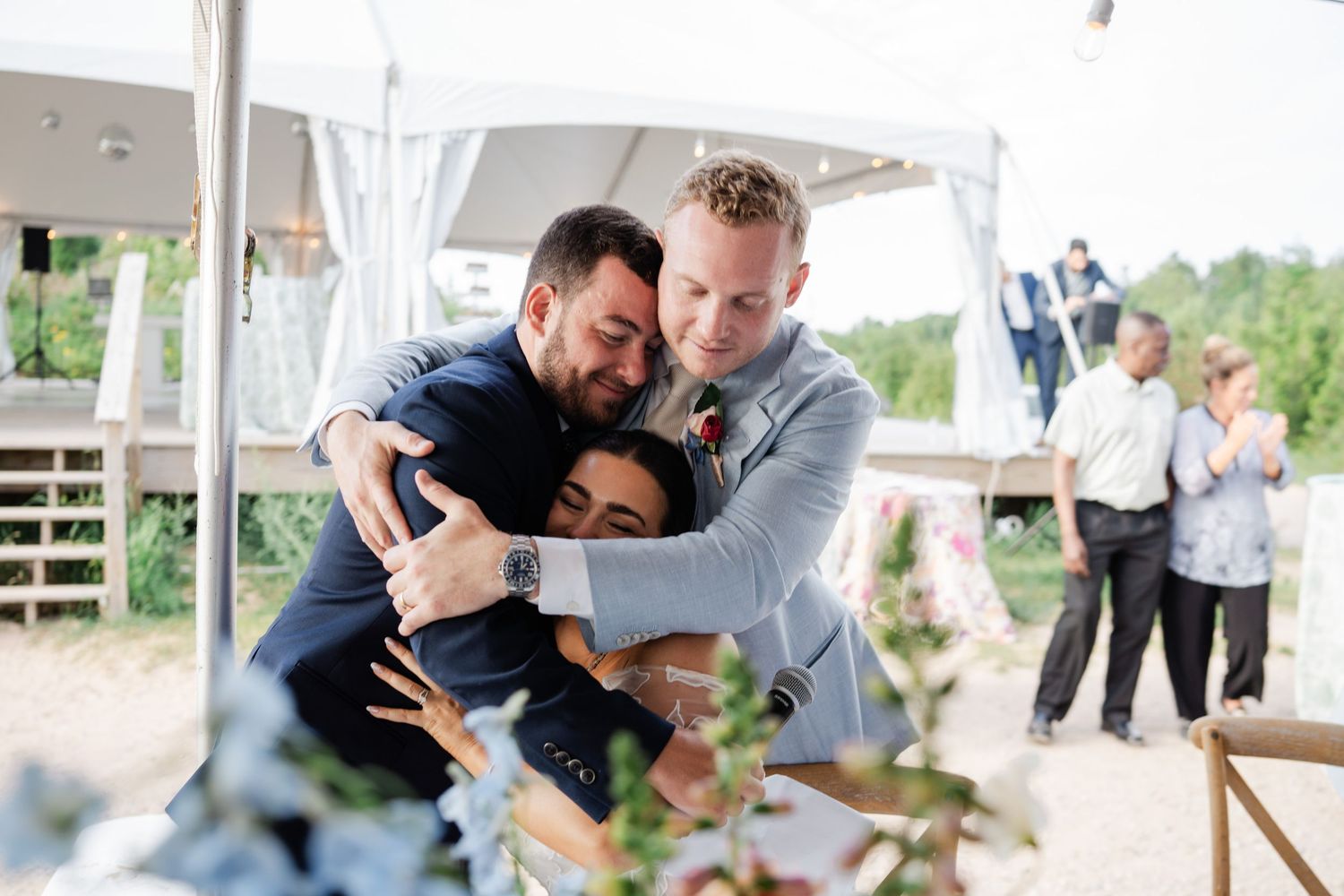 Emotional wedding moment as a groom shares a warm group hug with two guests at the reception.