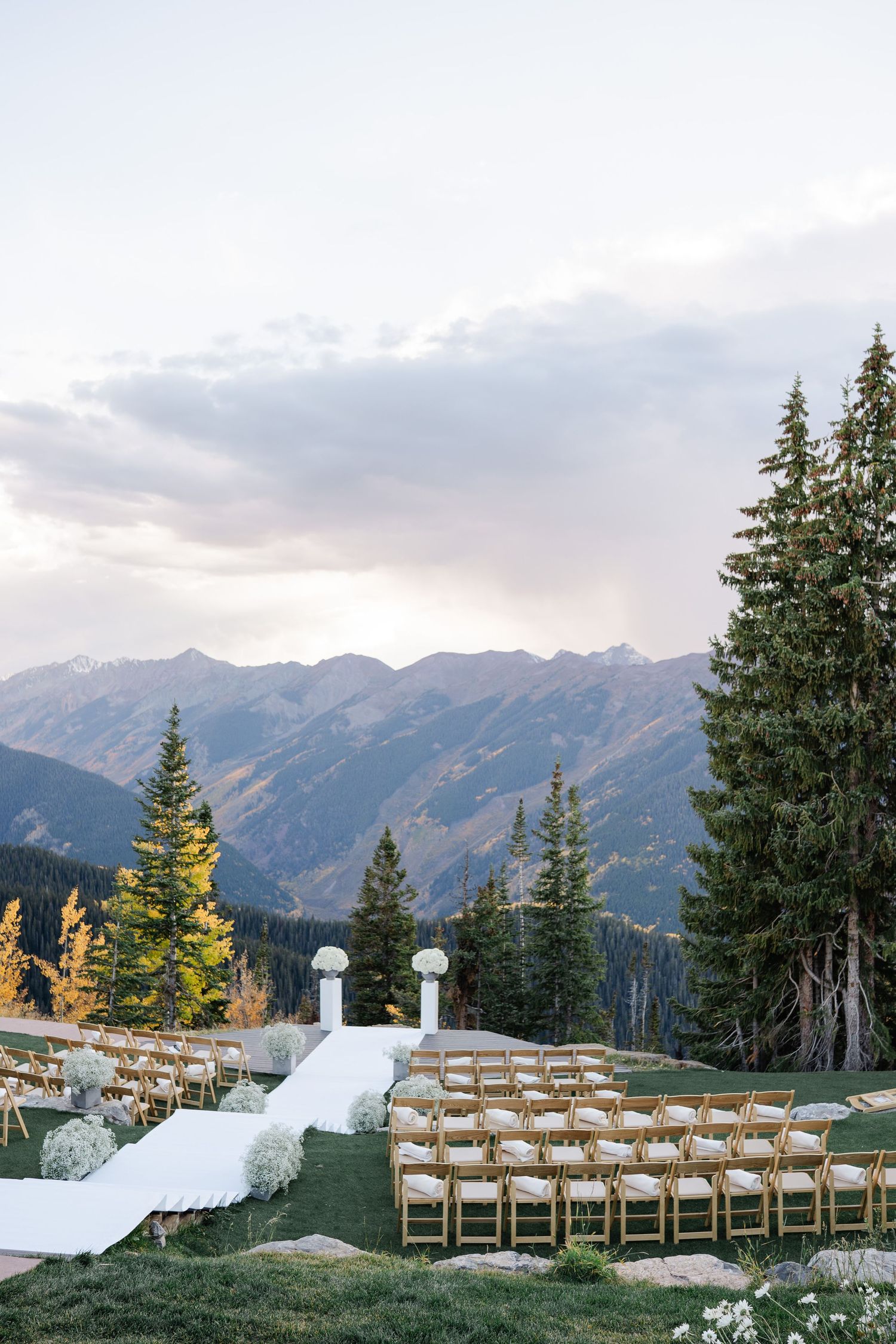 Outdoor mountain wedding ceremony setup with wooden chairs and white aisle against stunning peaks.
