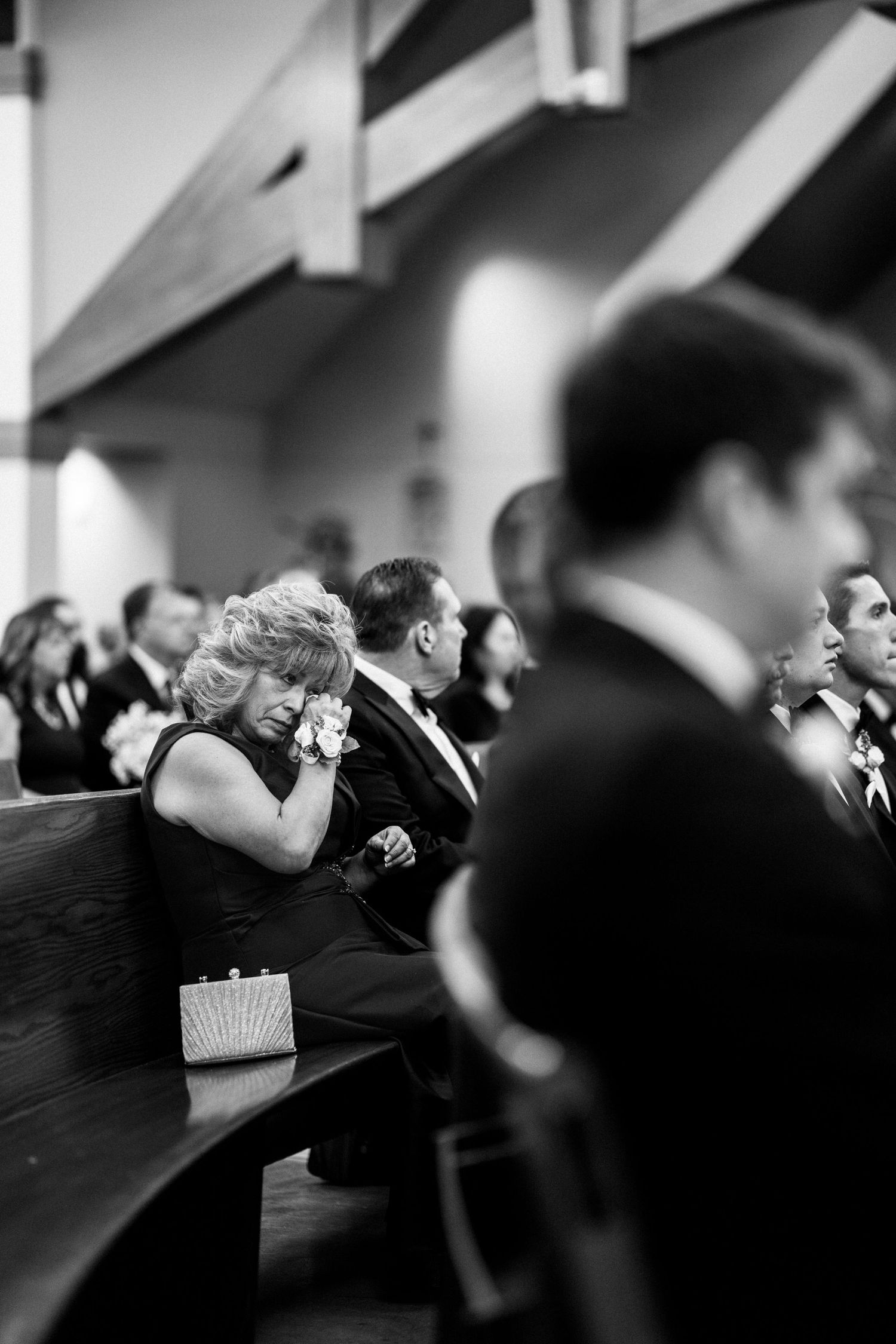 Emotional wedding guest crying in church pew during ceremony in black and white photo.