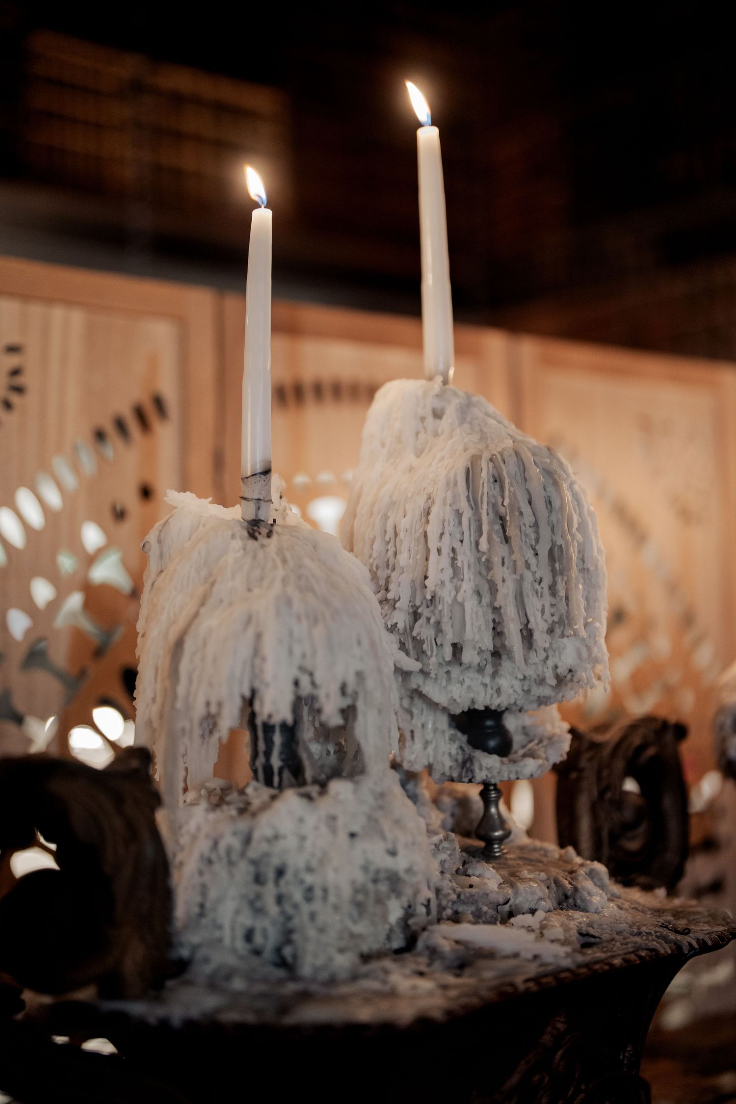 Two white taper candles burning on ornate candleholders draped in white wax at a dark romantic wedding reception.
