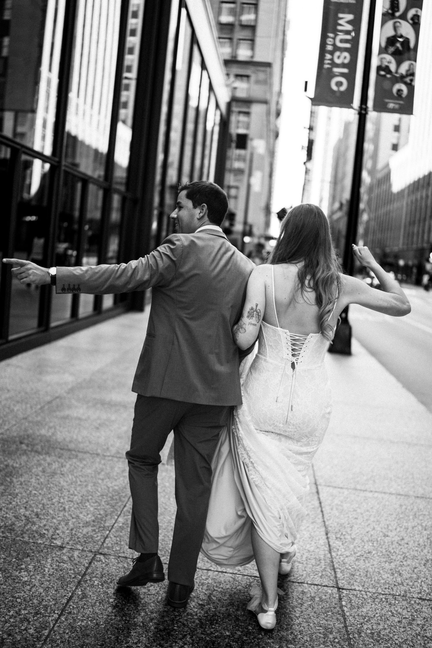 Black and white photo of bride and groom walking arm in arm down city street.
